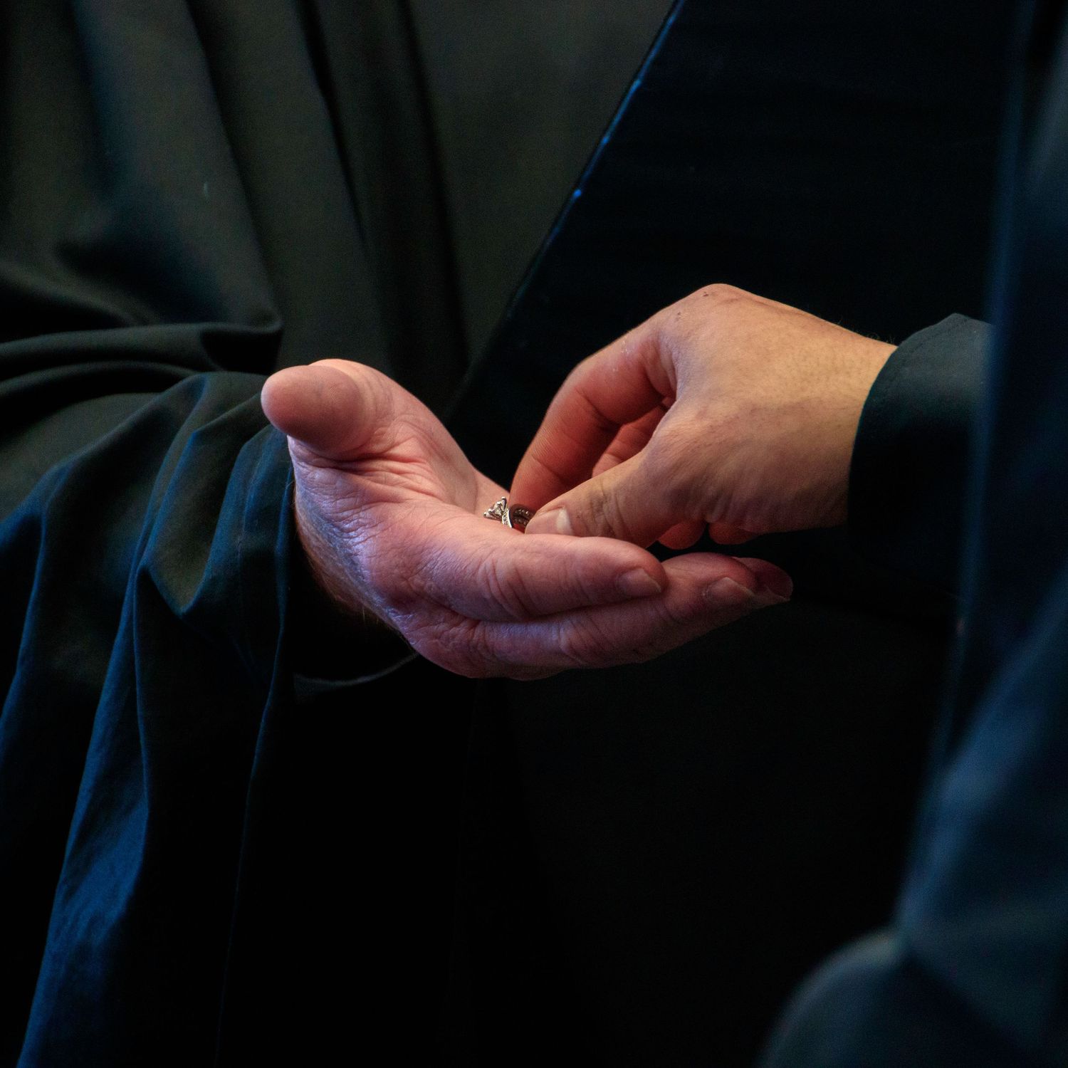 Close-up sequence of hands exchanging a small gold ring in dim lighting.