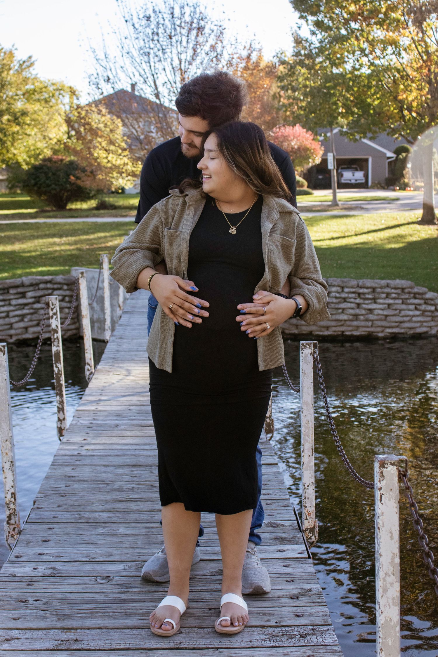 A couple sits together on a wooden dock by a lake during autumn.