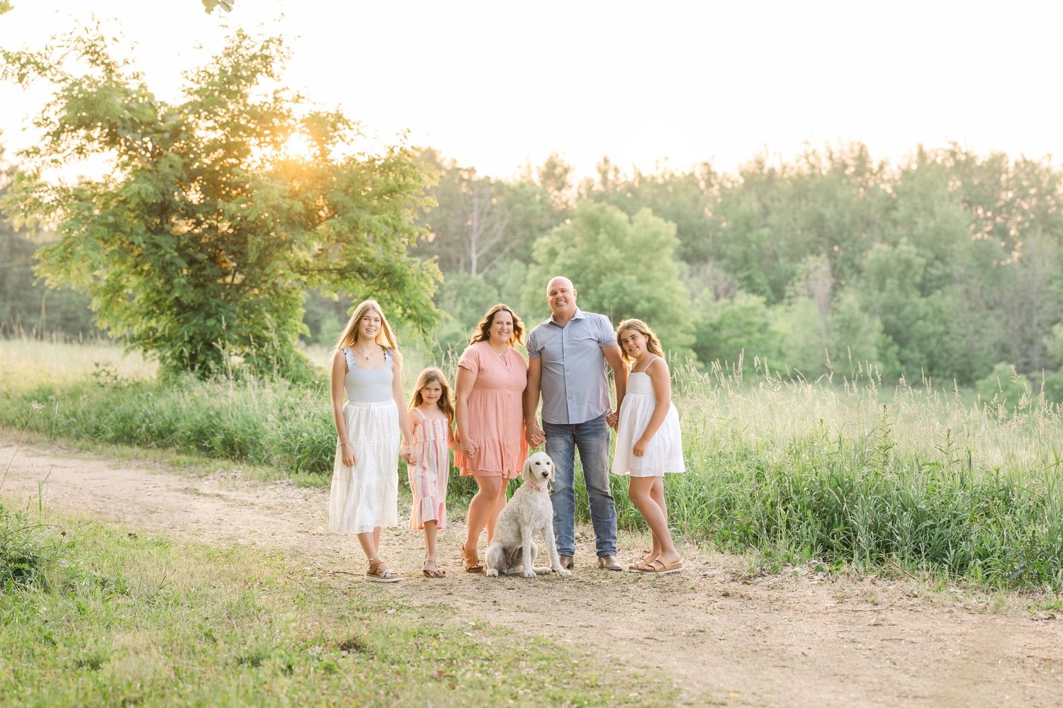 A candid family portrait on a sunlit dirt path surrounded by lush greenery.