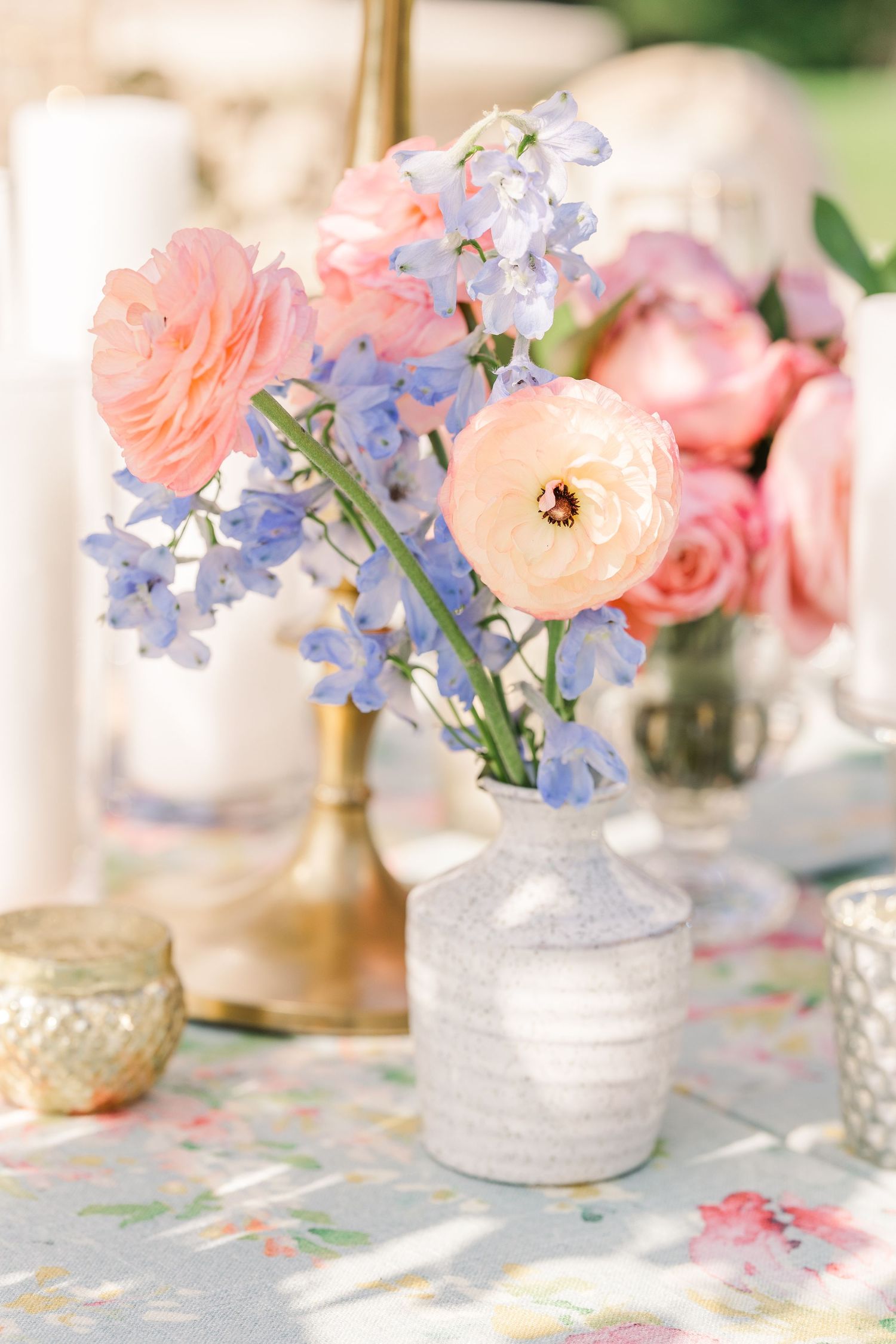 Delicate floral centerpiece with pink roses and blue delphiniums in frosted glass vase.