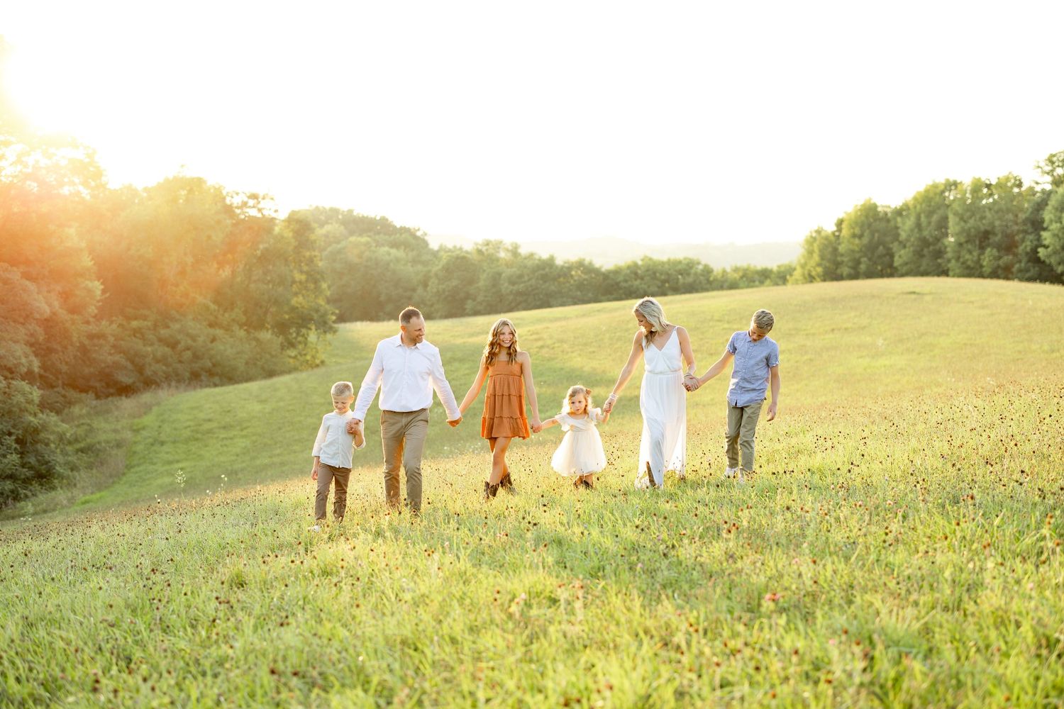 A family walks together through a sunlit meadow during golden hour.