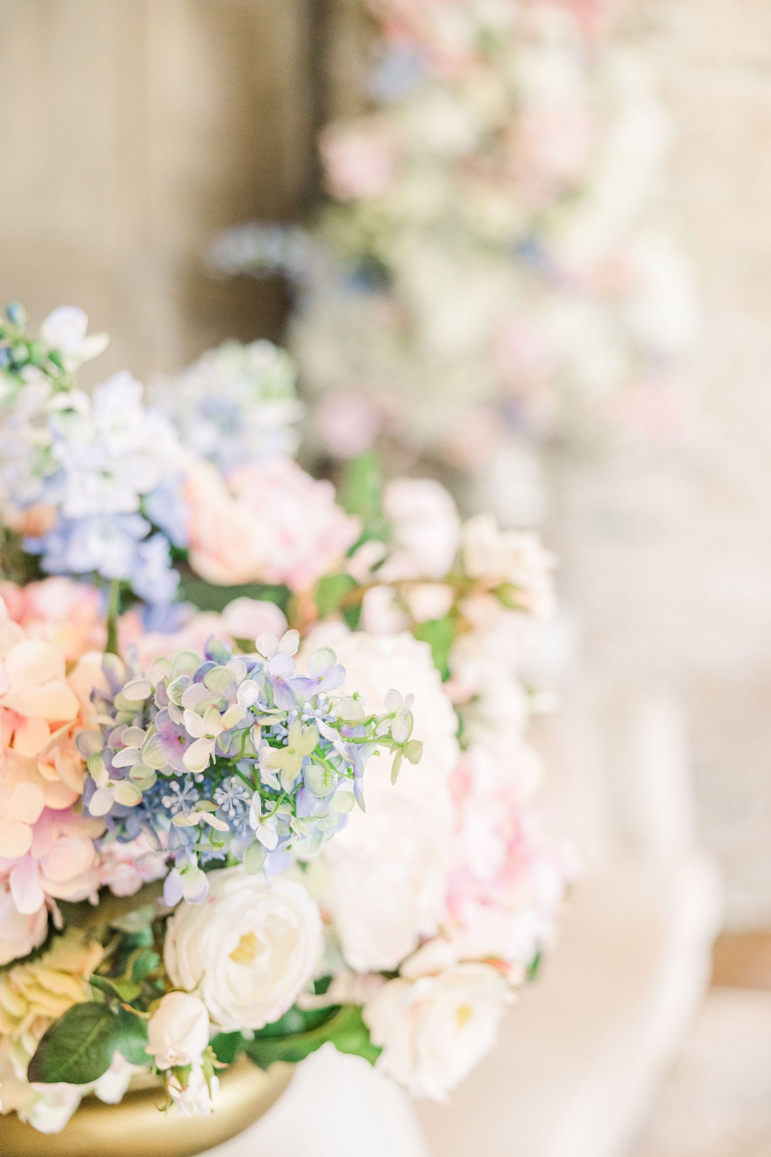 Elegant floral arrangement featuring pastel pink, blue and white blooms in a gold vase.