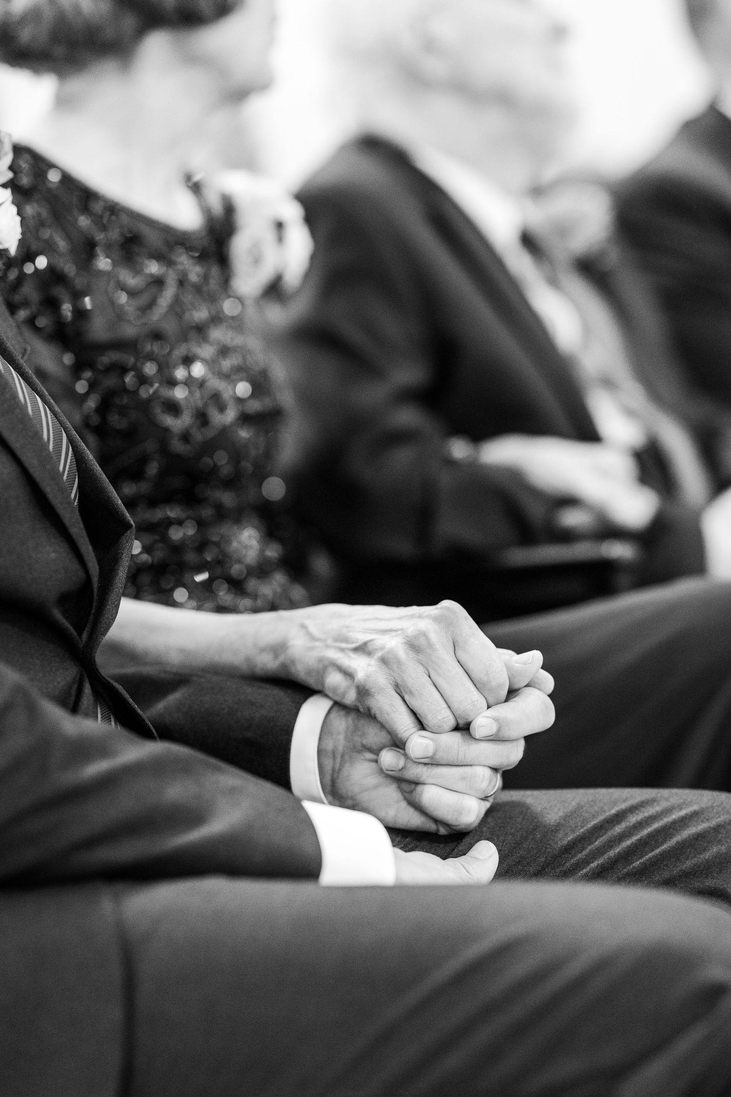A tender black and white moment of clasped hands during a wedding ceremony.