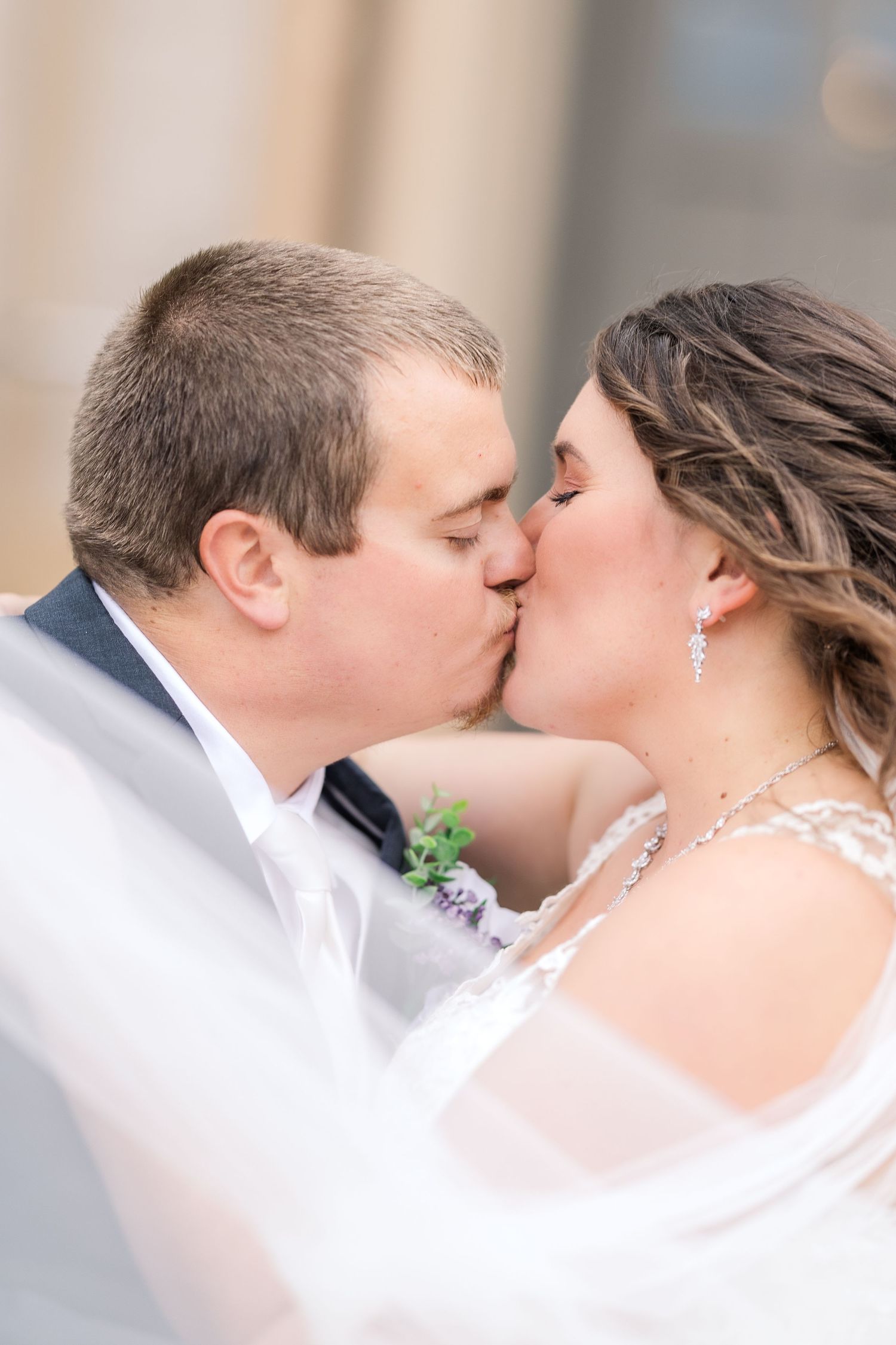 A romantic wedding kiss captured in soft natural light with the bride wearing a veil.
