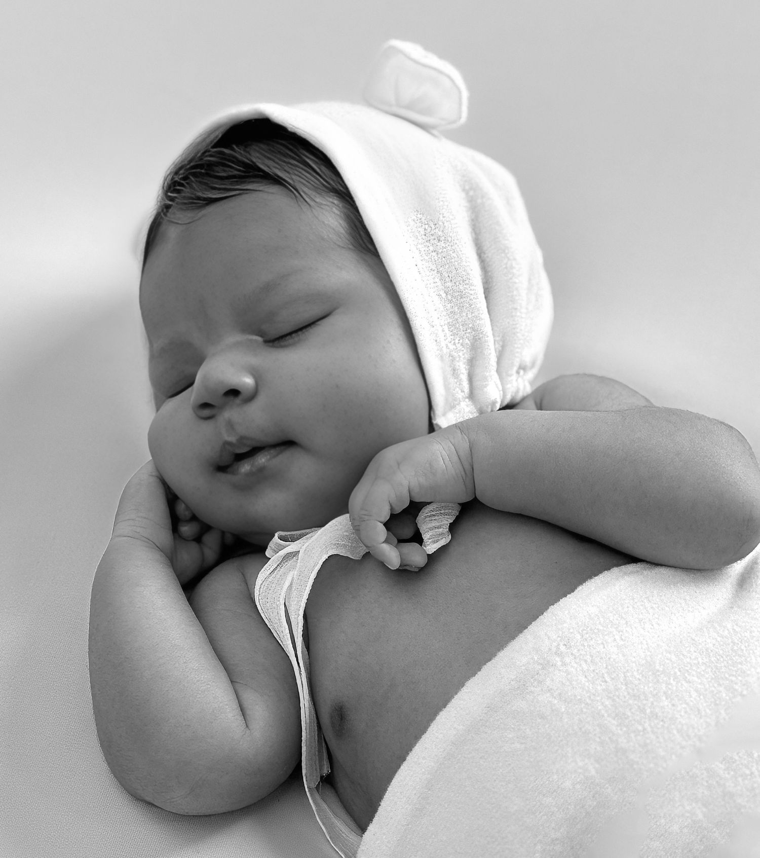 A series of black and white photographs showing a sleeping newborn baby in soft white blankets. Newborn fotografie Almere
