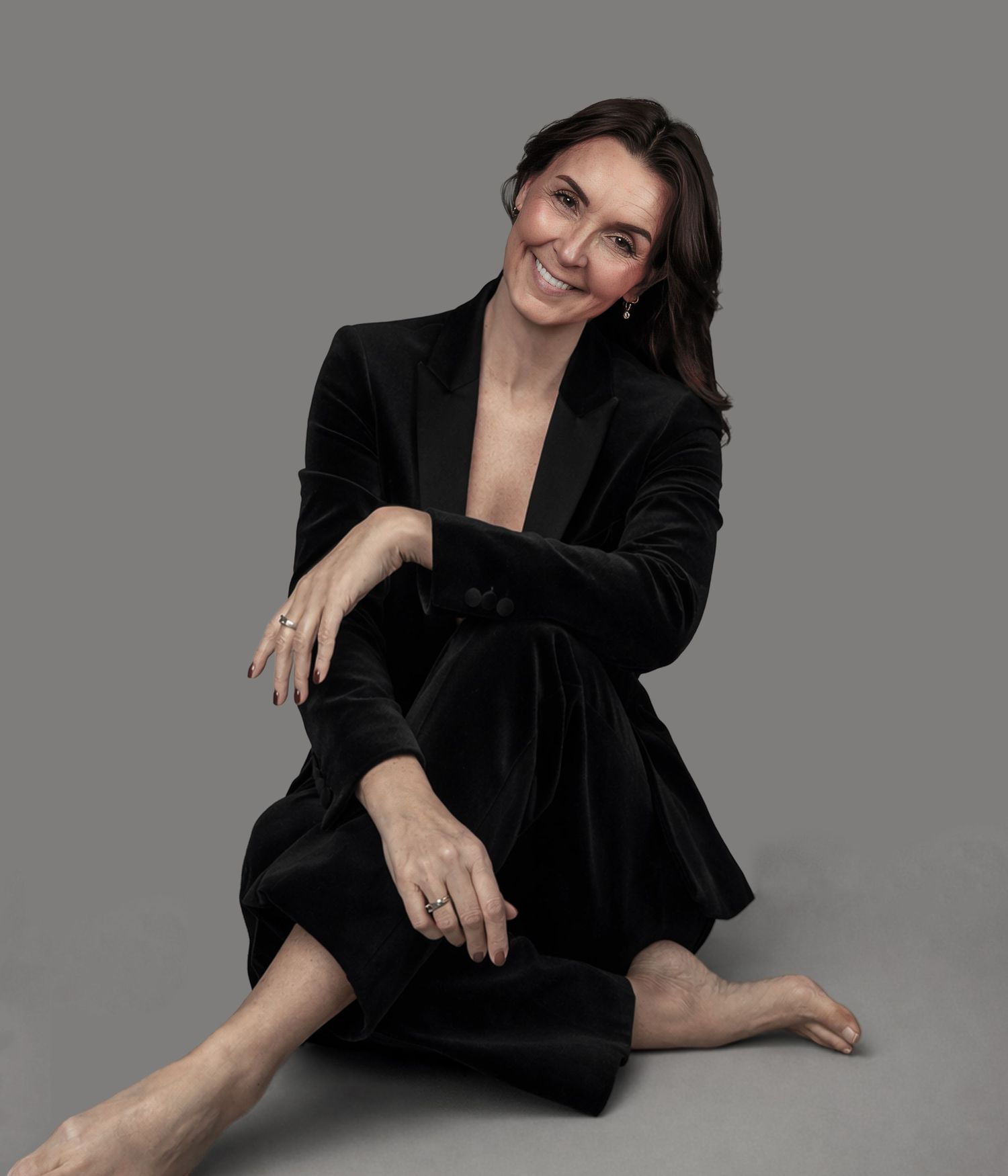 Professional fashion portrait of someone in a black blazer posing artistically against a gray studio backdrop.