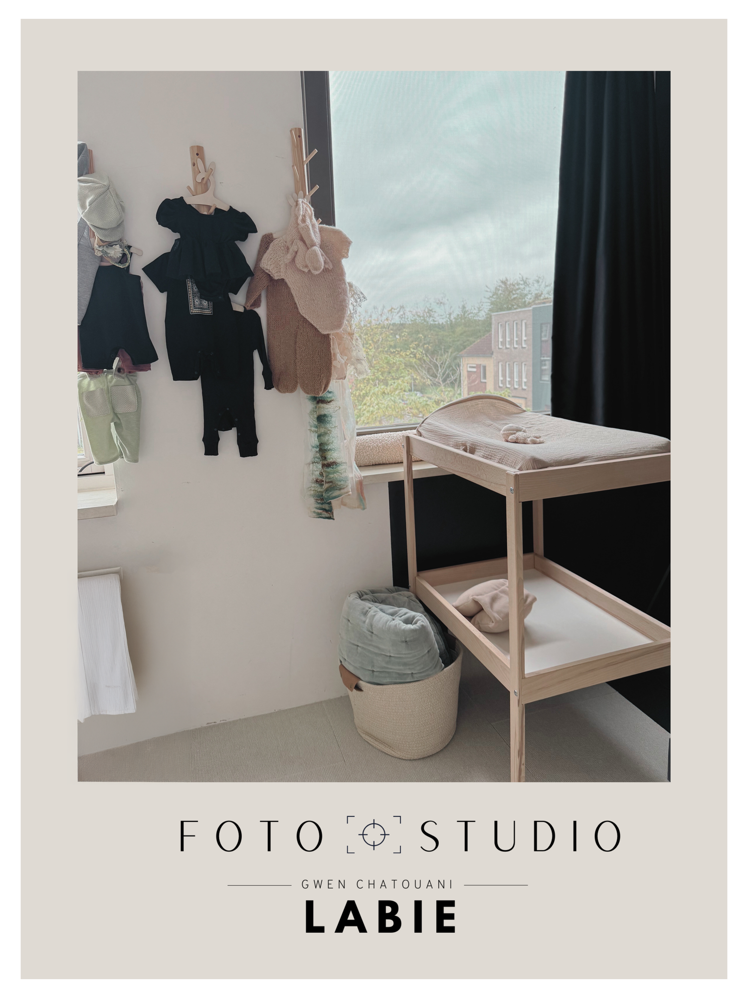Minimalist studio space with hanging clothes, wooden furniture, and soft neutral decor against white walls.