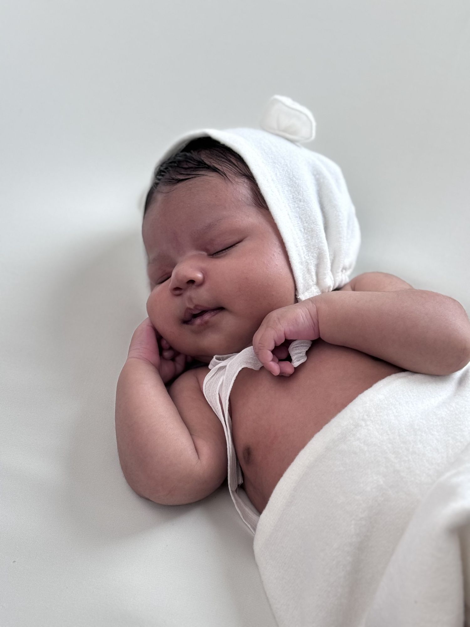 Peaceful sleeping newborn baby wearing white cap and swaddled in soft white blanket.