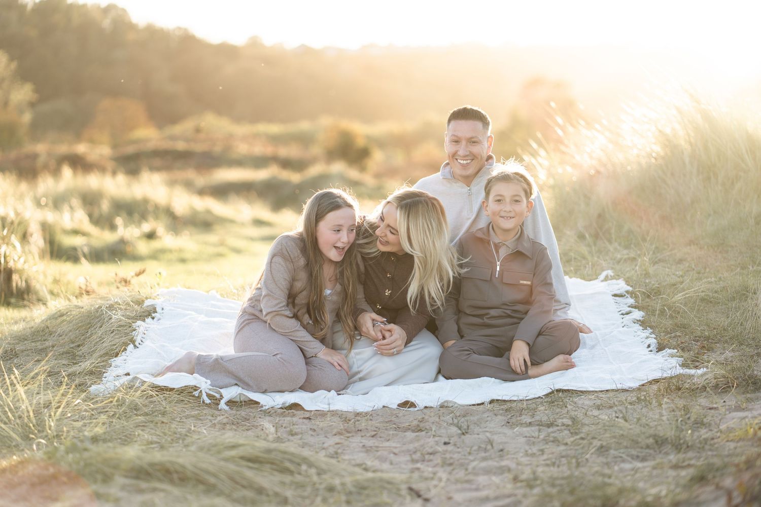 Couple laying together on white blanket in sunlit field during golden hour sunset.