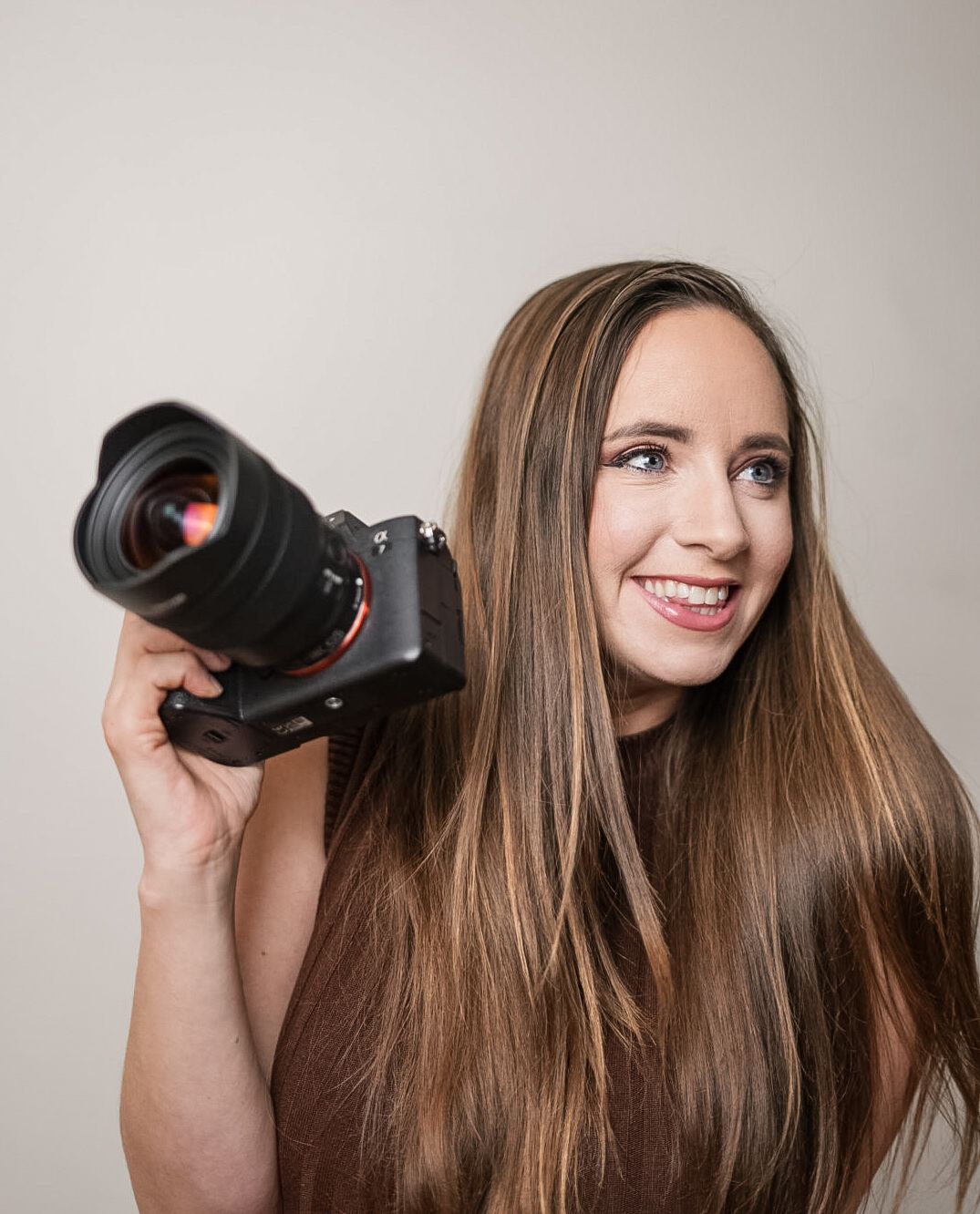 A photographer with long brown hair holds up a camera lens while posing in a series of expressive shots.