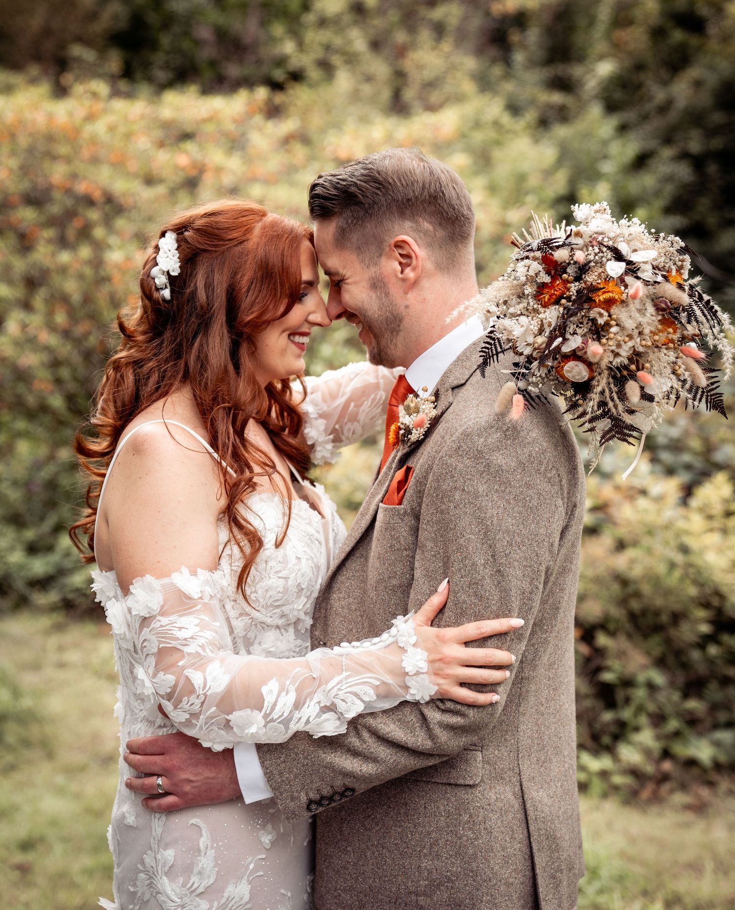 A loving couple shares an intimate moment outdoors at their wedding celebration with autumn floral decor and earthy tones.