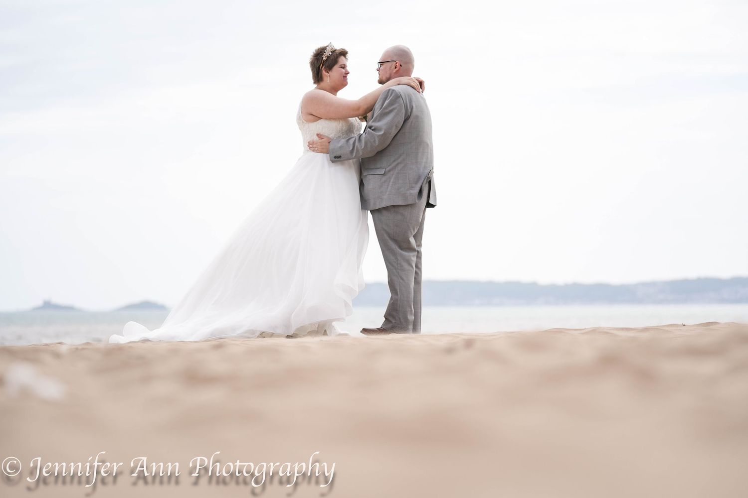 A couple embraces and dances intimately on a serene beach at sunset with mountains in the distance.