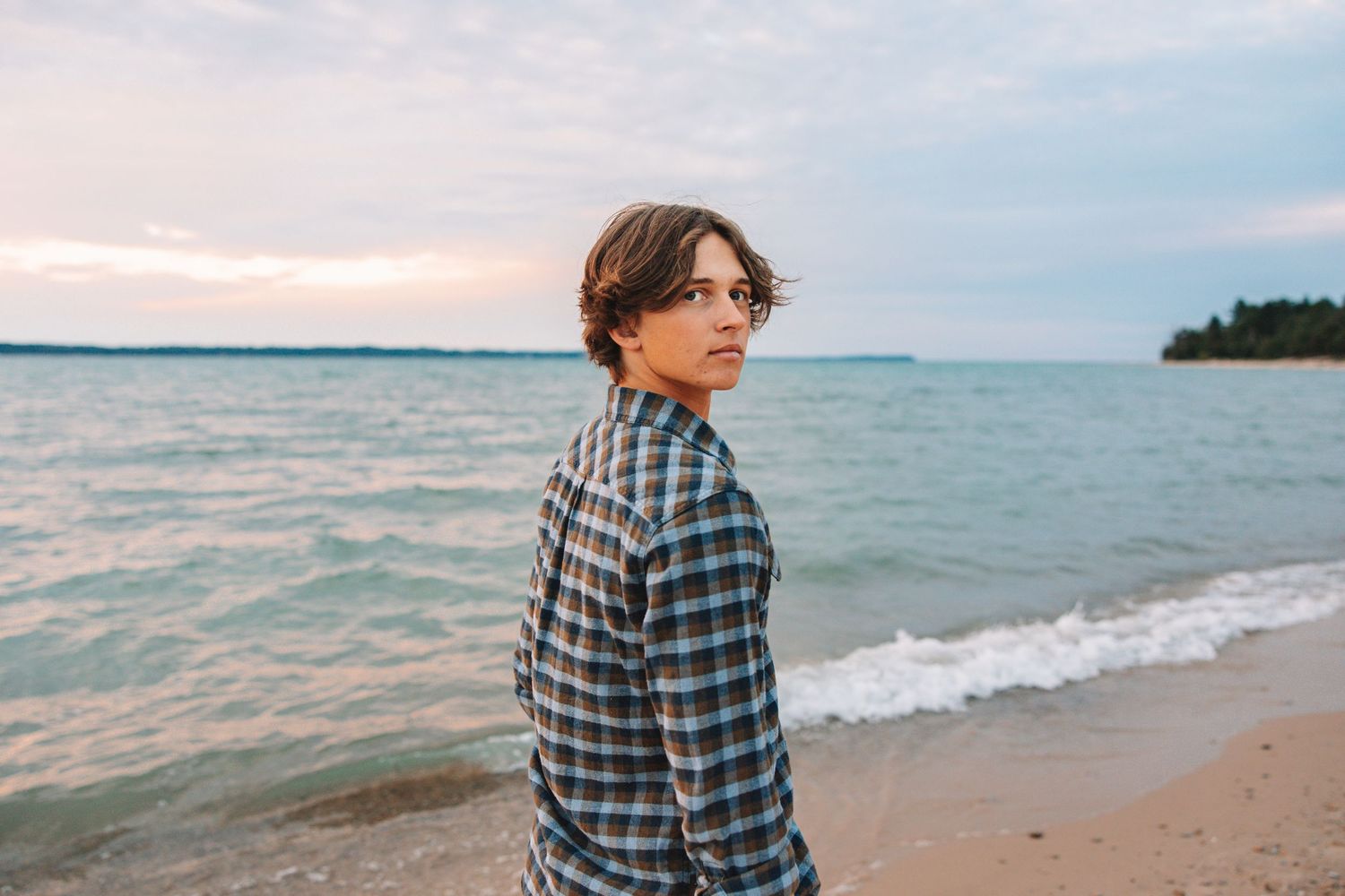 Guy senior poses for photo on beach in Traverse City, Michigan for a photoshoot for high school senior photos.