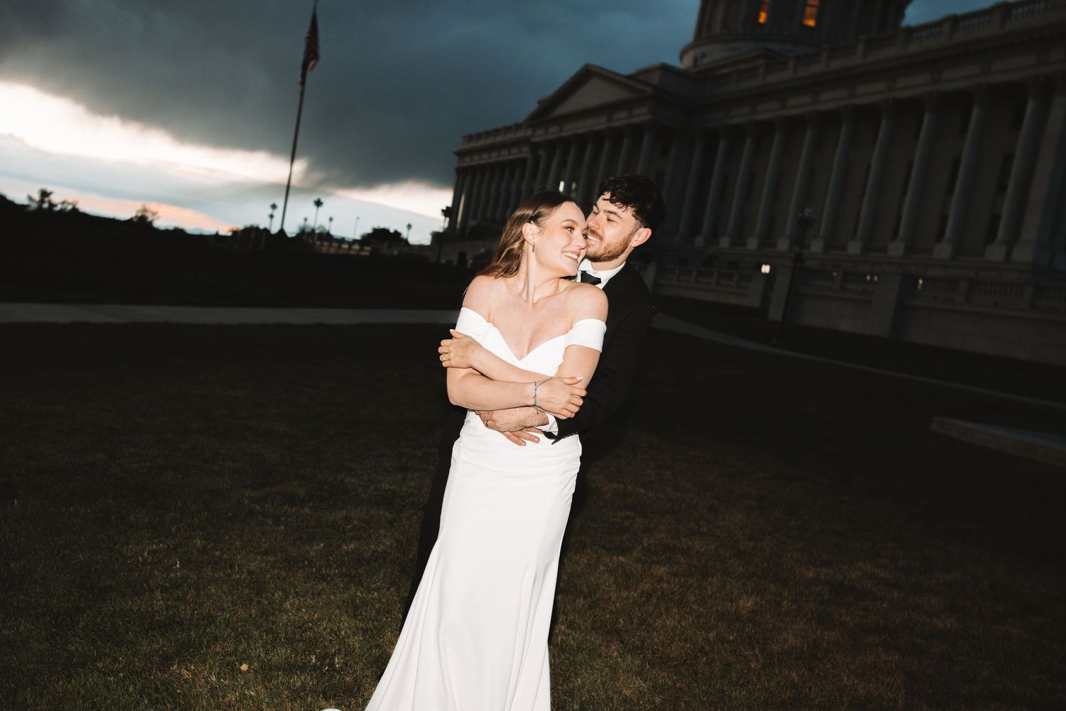 Bride and groom embracing outdoors at the Utah State Capitol under dramatic evening skies