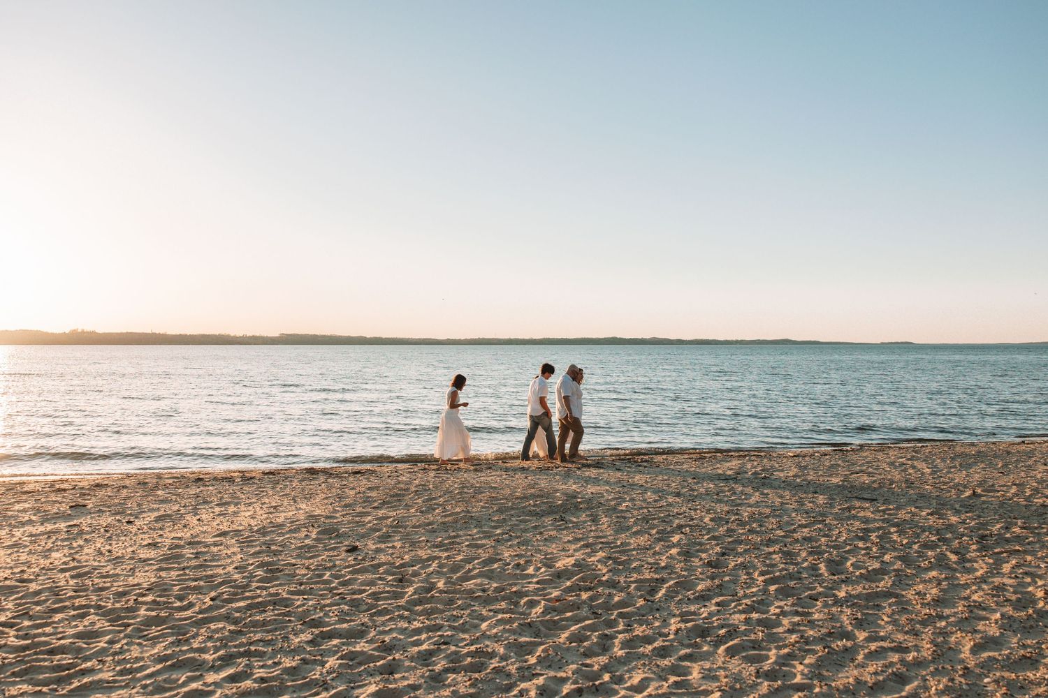 Family walking along a wide beach shoreline with open water and soft evening light