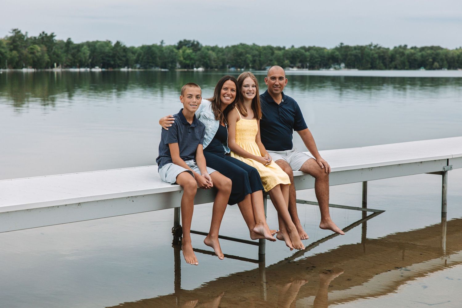 Family sitting together on a dock by the water during a summer family photo session In Traverse City, Michigan