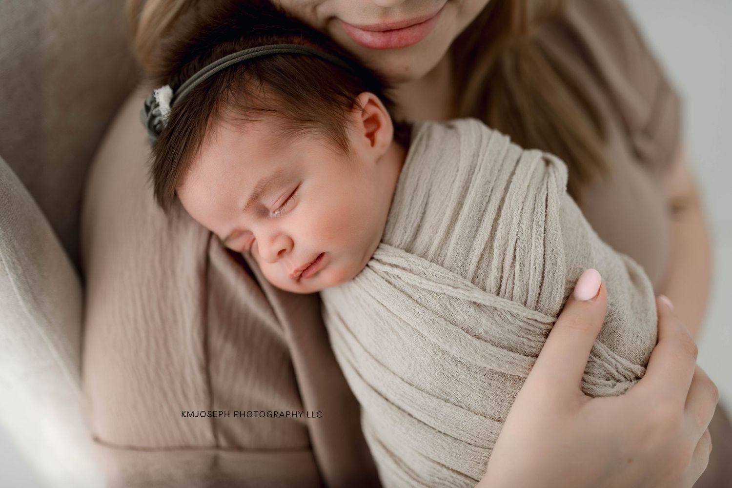 Newborn baby wrapped in soft gray swaddle being gently held.