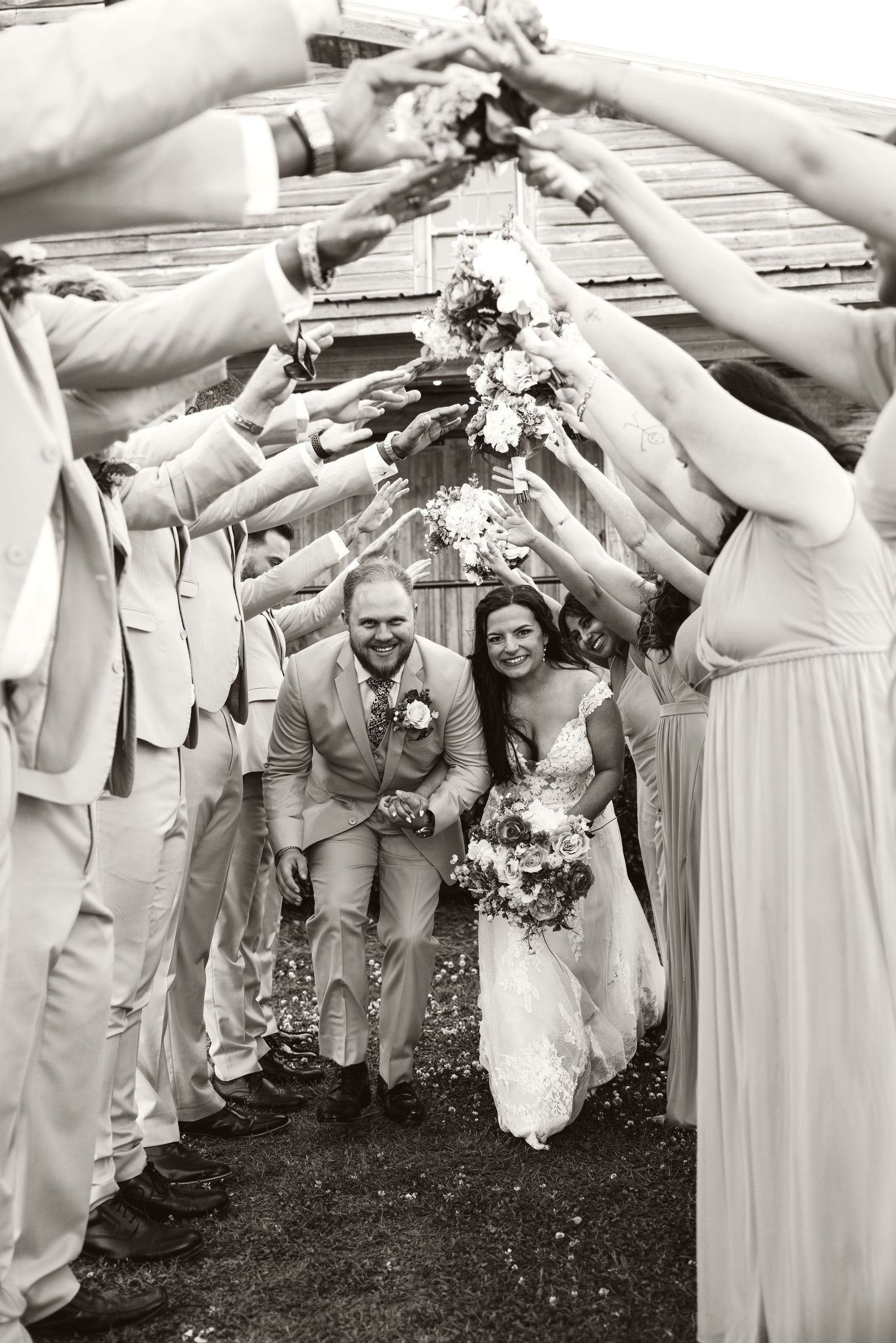 Wedding party forms a tunnel with raised arms as newlyweds pass underneath in joyful celebration.