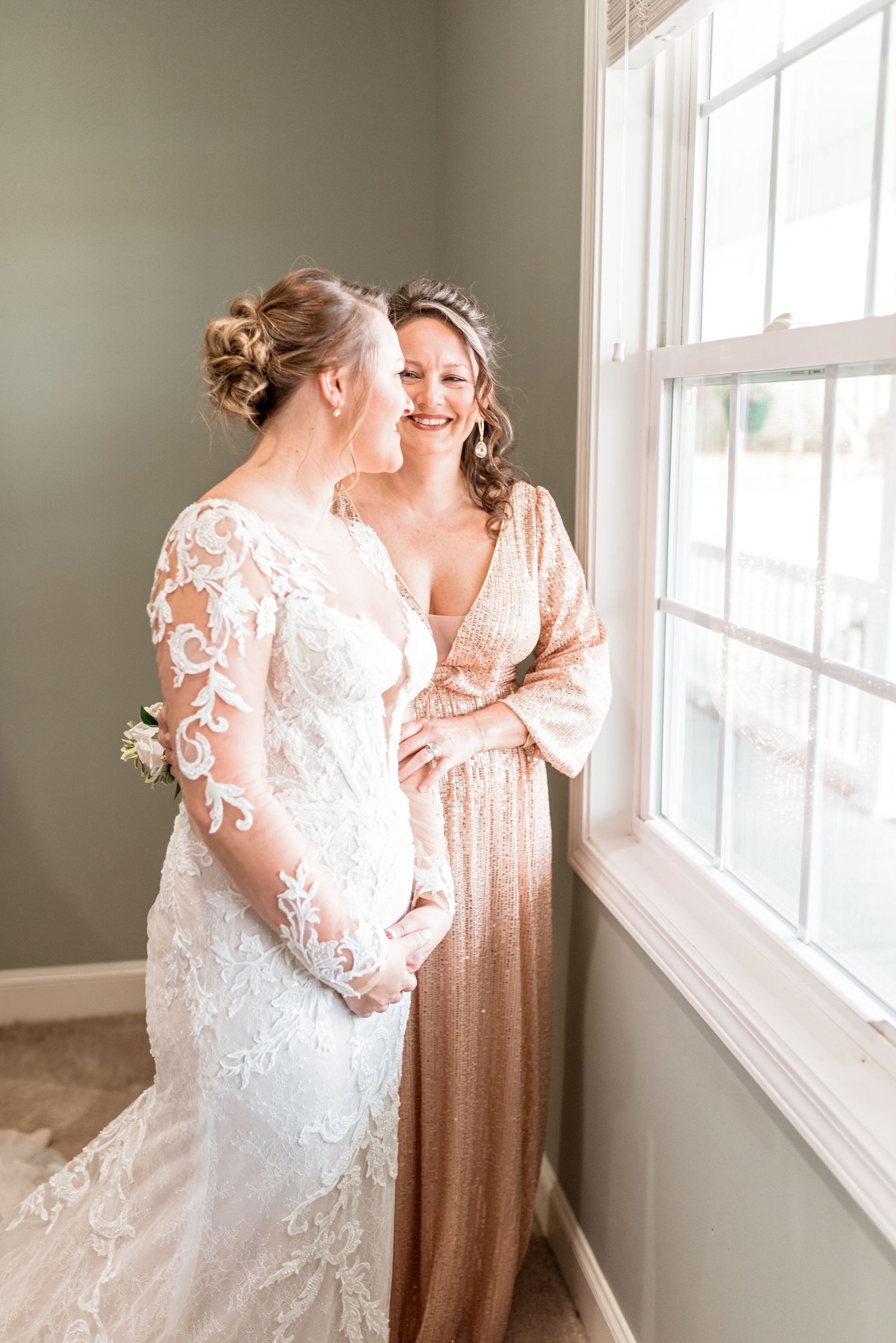 Wedding scene by window with elegant lace dress and rose gold bridesmaid gown.