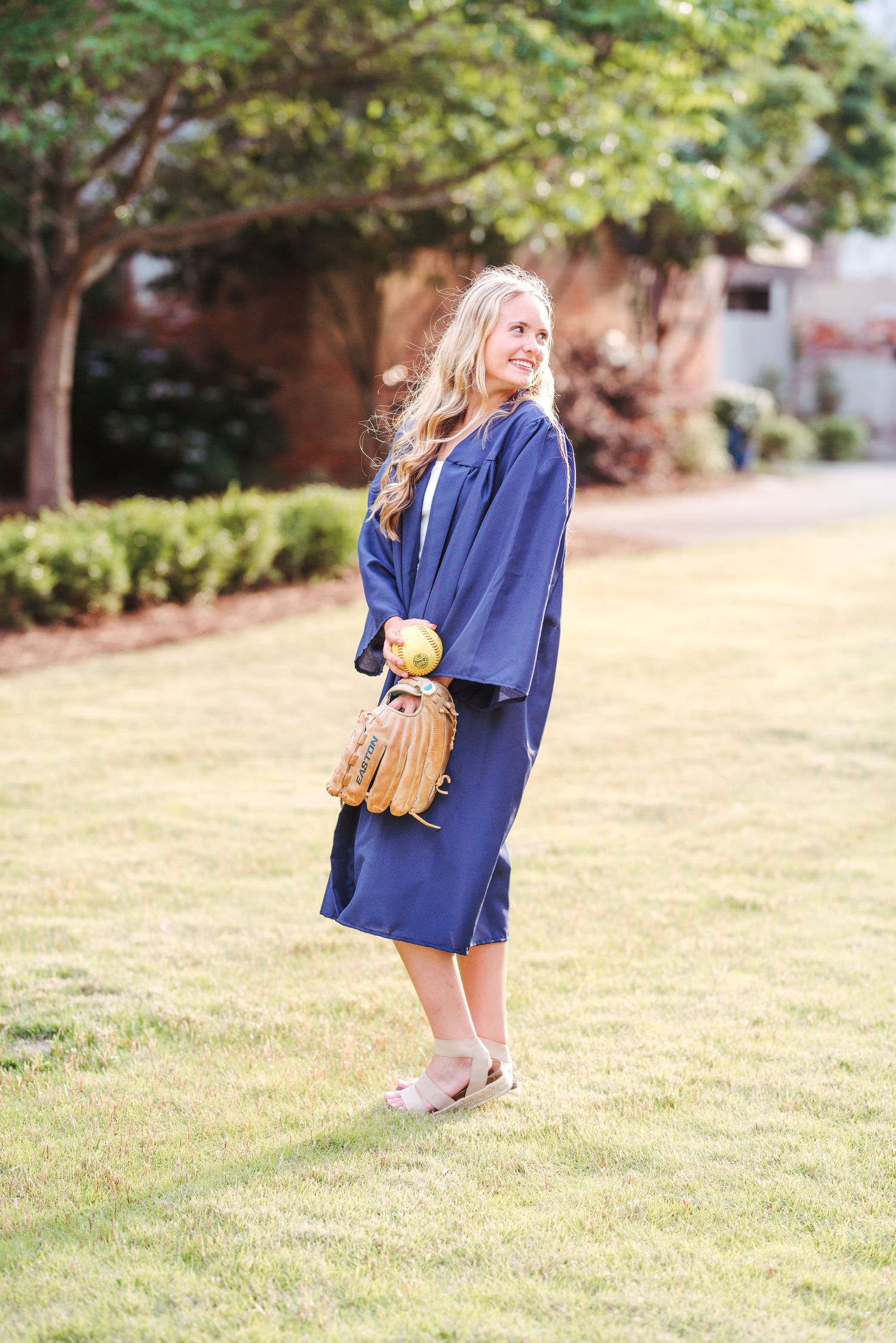 A graduate in a navy blue outfit poses outdoors on a grassy lawn.
