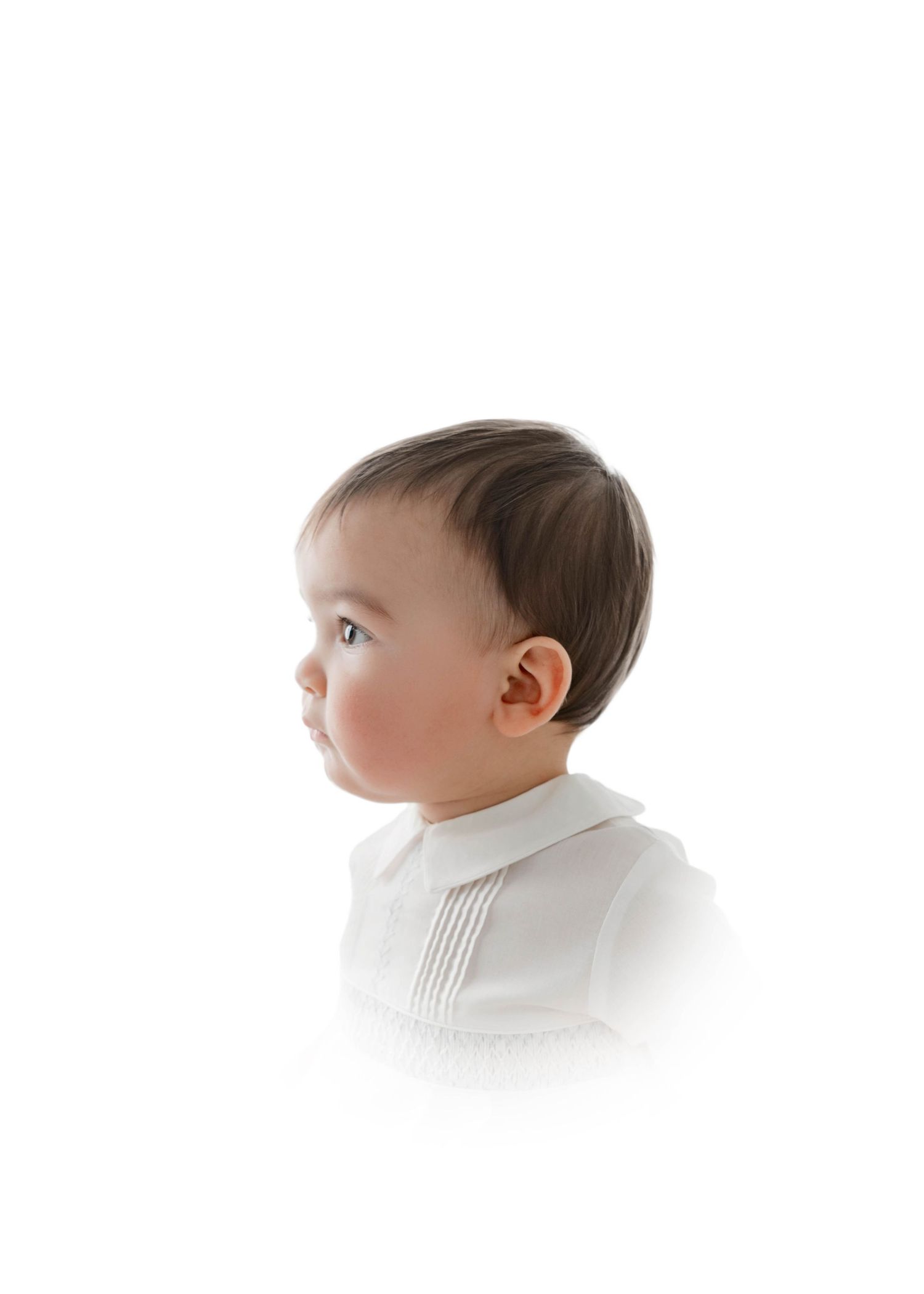 Side profile of a baby with dark hair wearing a white collared shirt against a white background.