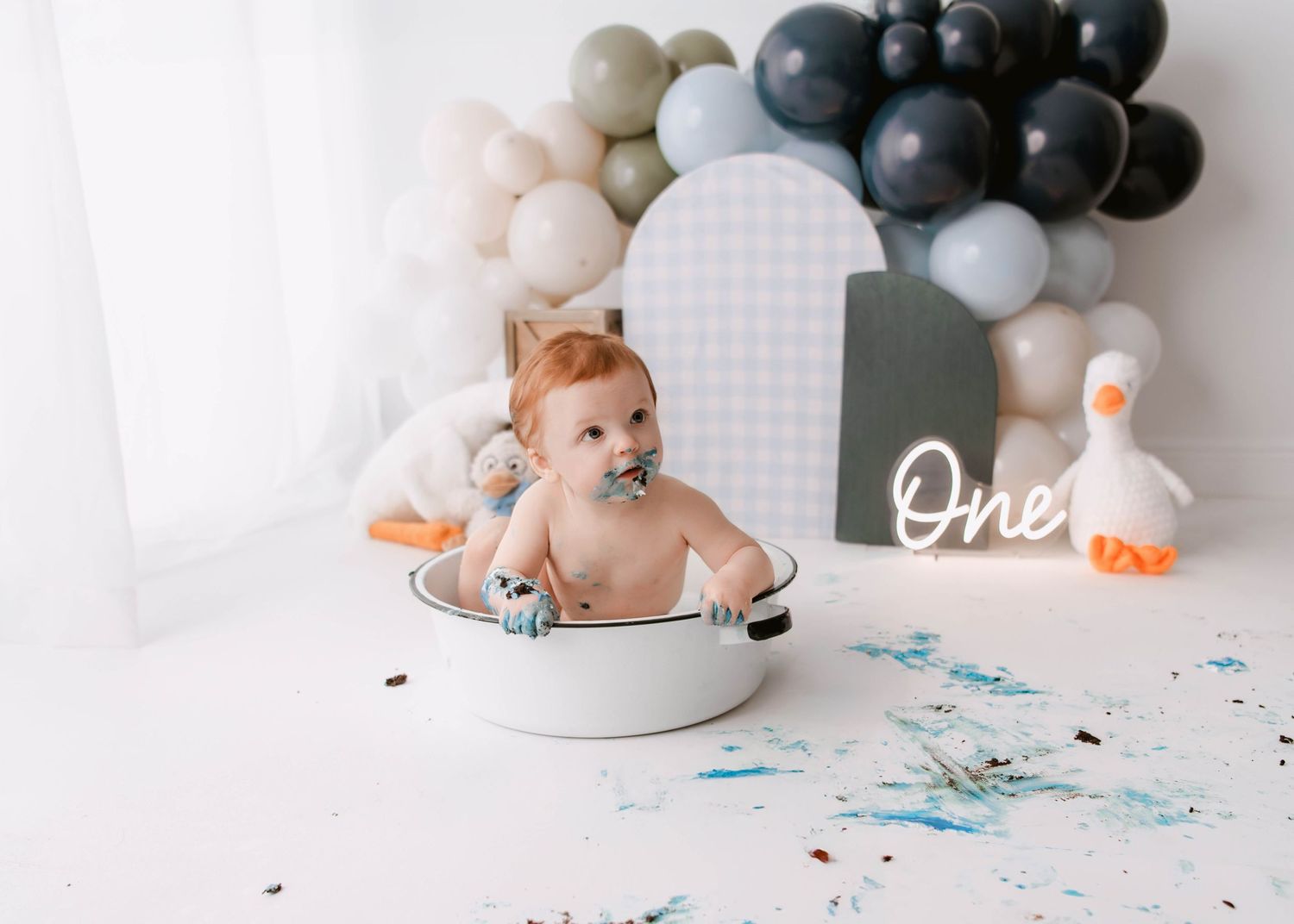 First birthday cake smash scene with black and gray balloon arch and white decorations.