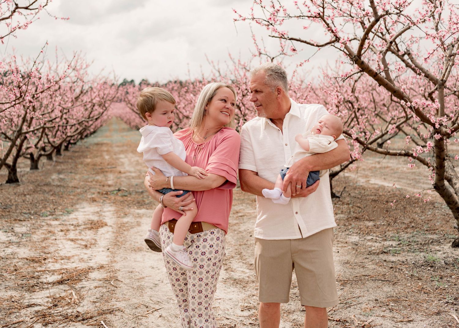 Group portrait in a peach orchard with blossoming trees in soft, warm tones.