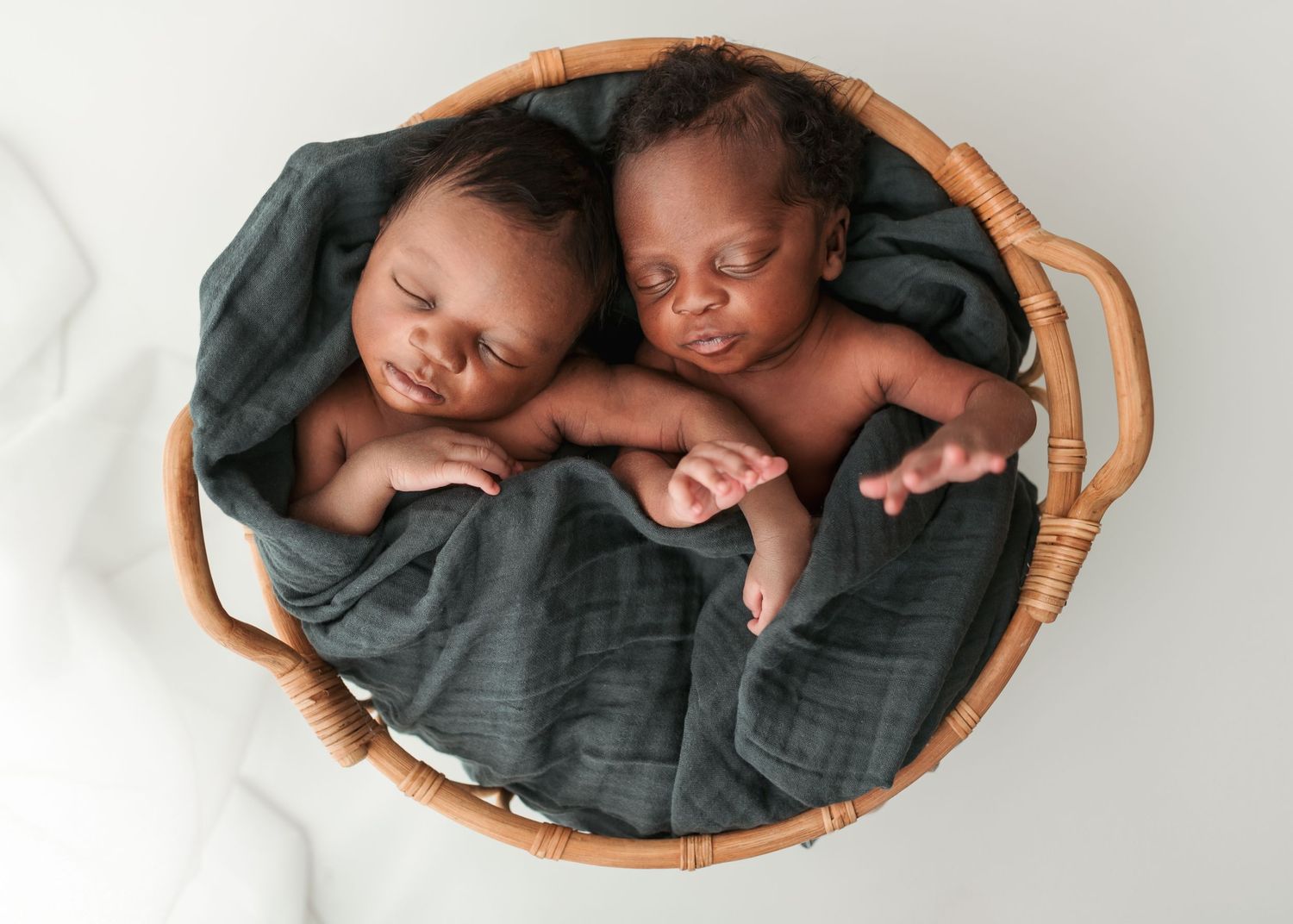 Two sleeping newborn babies posed together in a round wicker basket with blanket during studio newborn session in Florence, SC.