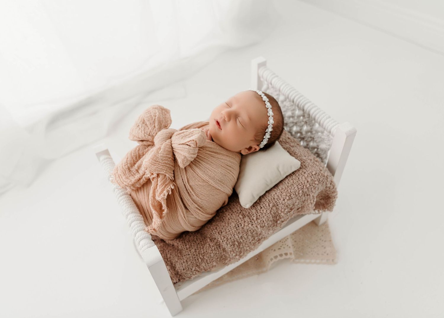 Newborn baby sleeping peacefully on soft beige blankets in natural light.
