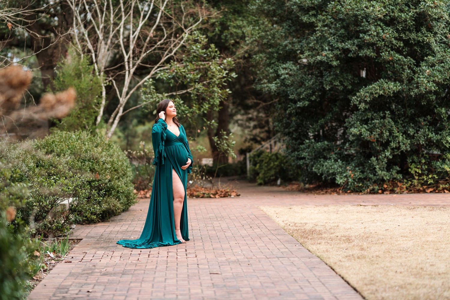 Elegant maternity photo of a woman in a flowing teal dress outdoors.