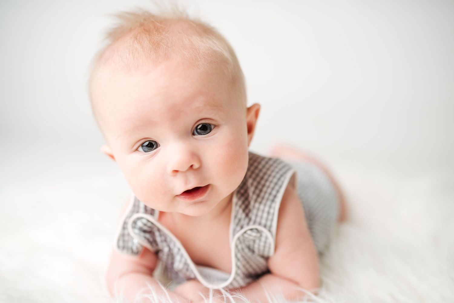 Baby in gray outfit smiling during professional photo session with white background.
