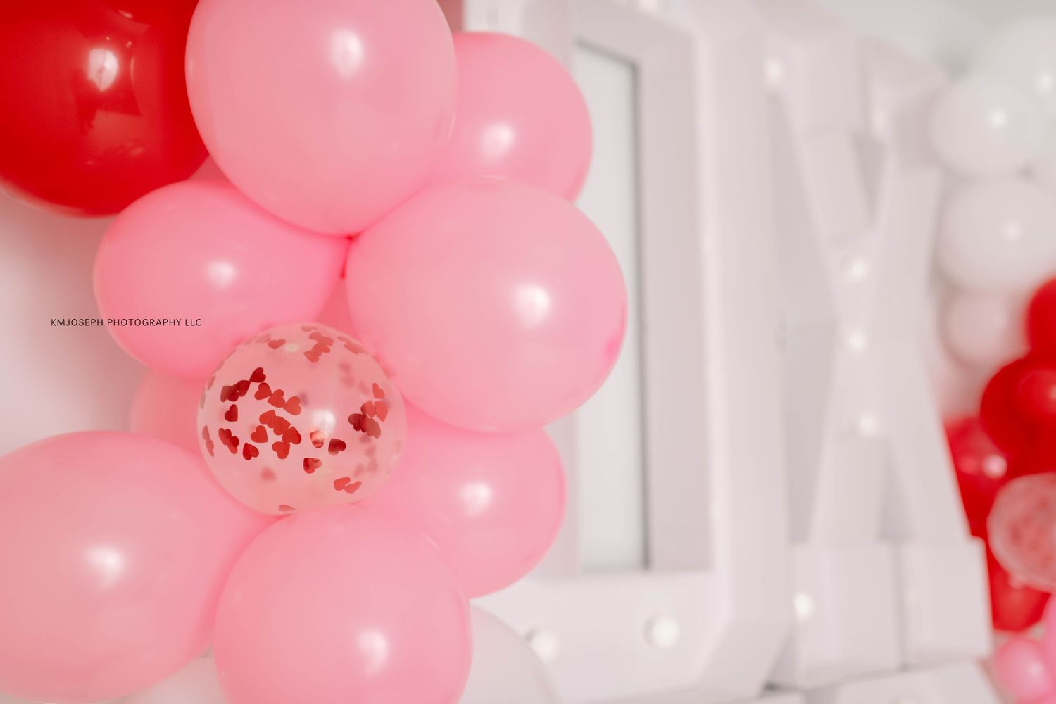 Pink and red balloon arch installation against a white backdrop.