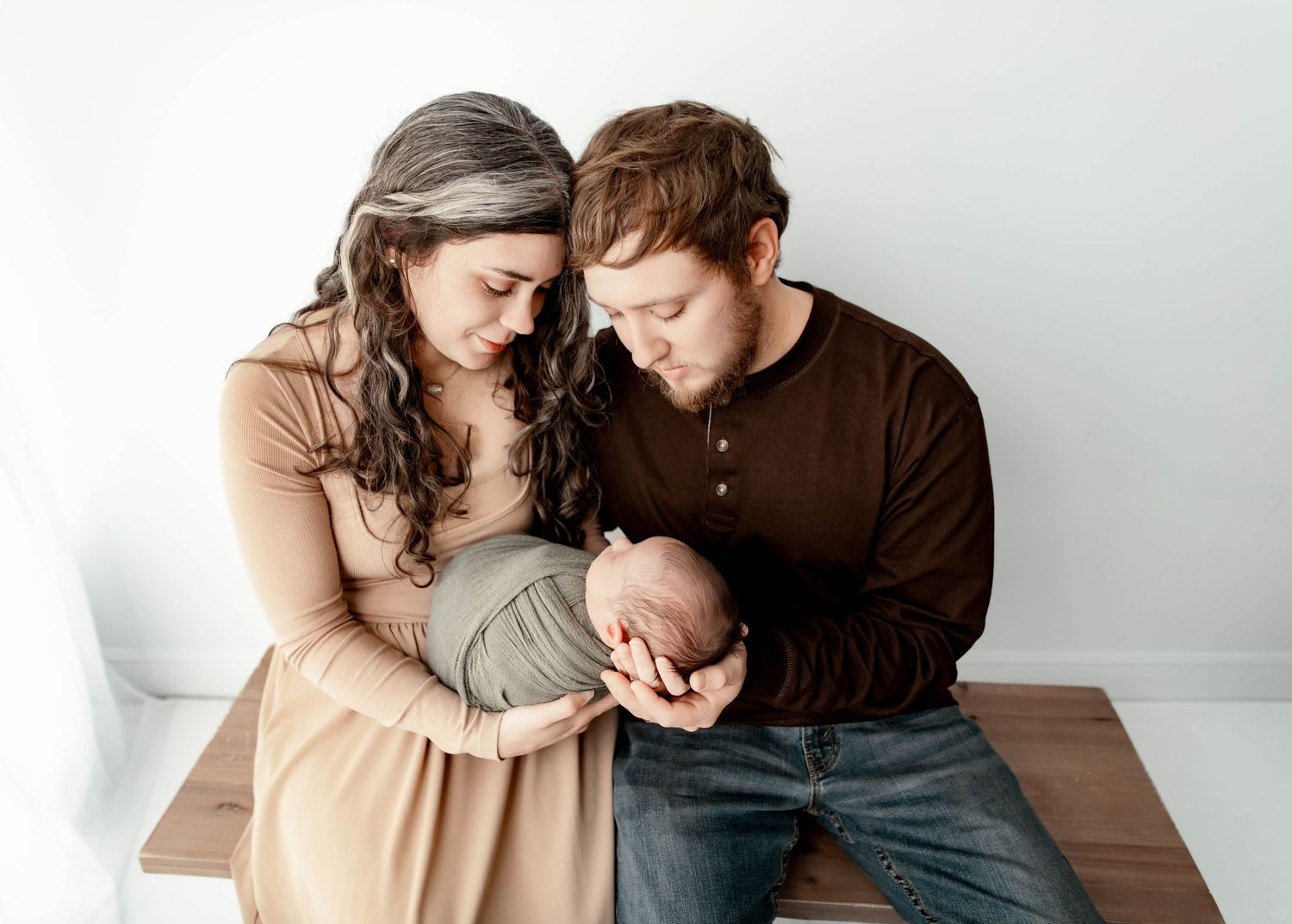 New parents tenderly gaze at their newborn baby during a professional studio portrait session.