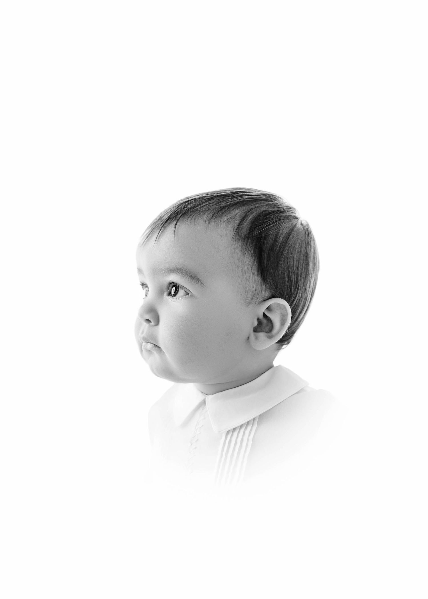 Black and white portrait of a young toddler with short dark hair wearing a white collared shirt, looking upward.