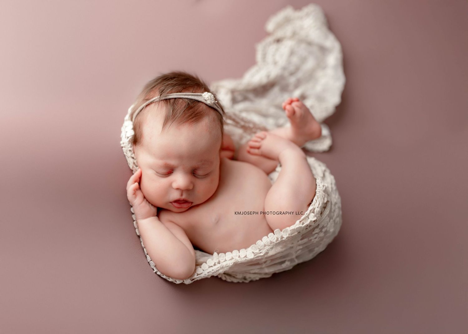Sleeping newborn posed on pink backdrop with delicate white wrap.