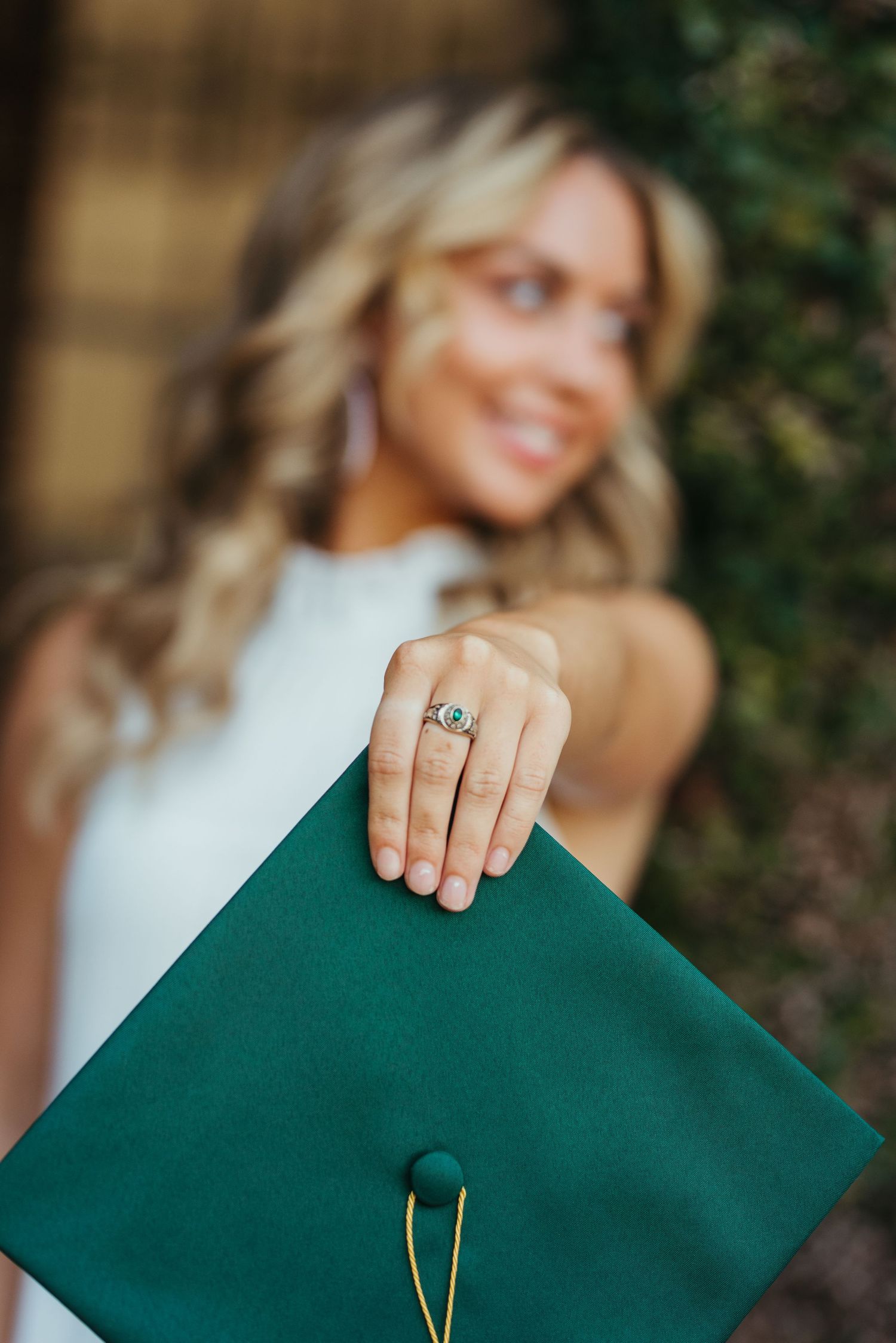 A graduate displays their graduation cap and ring while wearing a white dress.