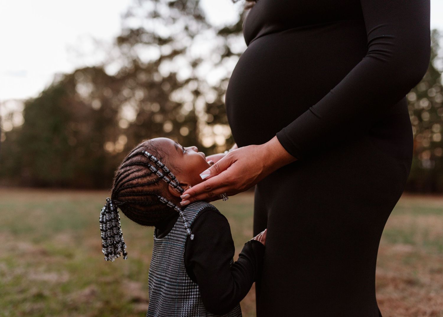 Close-up of hands holding a small knit hat against a pregnant belly in a black dress.