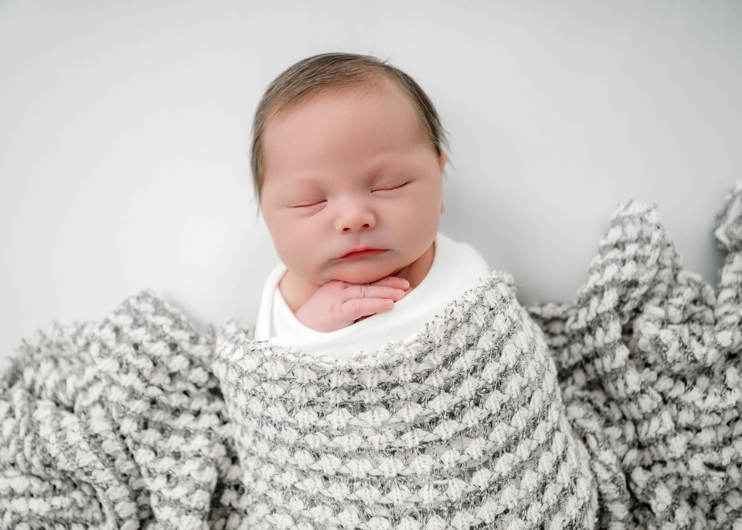 Peaceful newborn baby sleeping wrapped in a soft gray knit blanket on a white background.