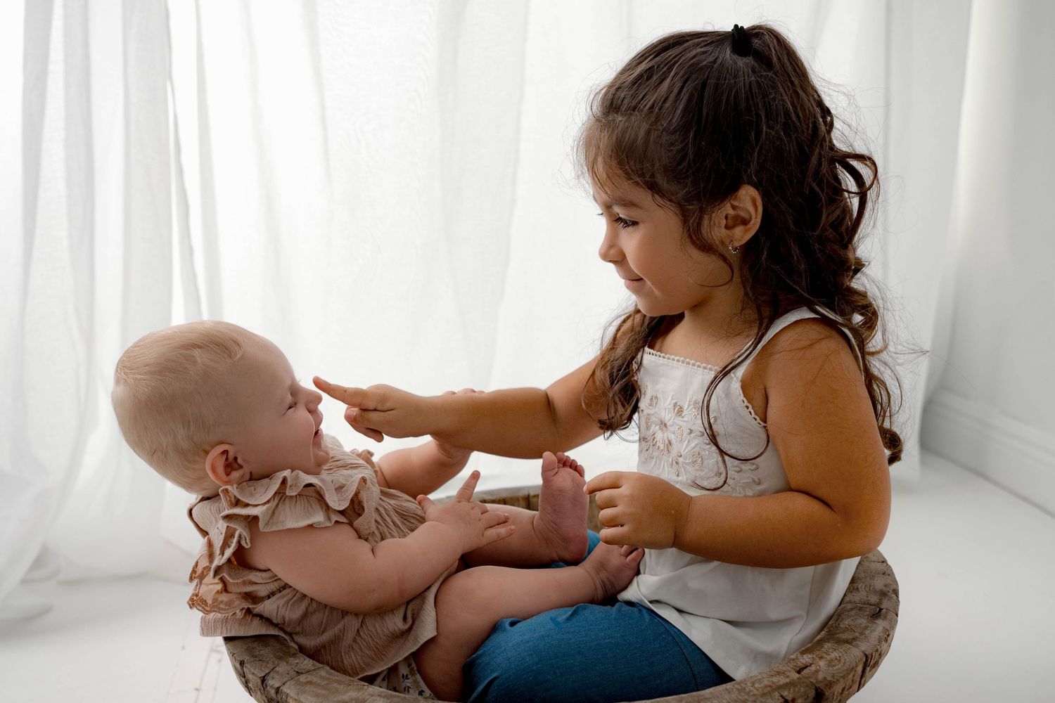 Two children interacting and playing together against white curtain background.