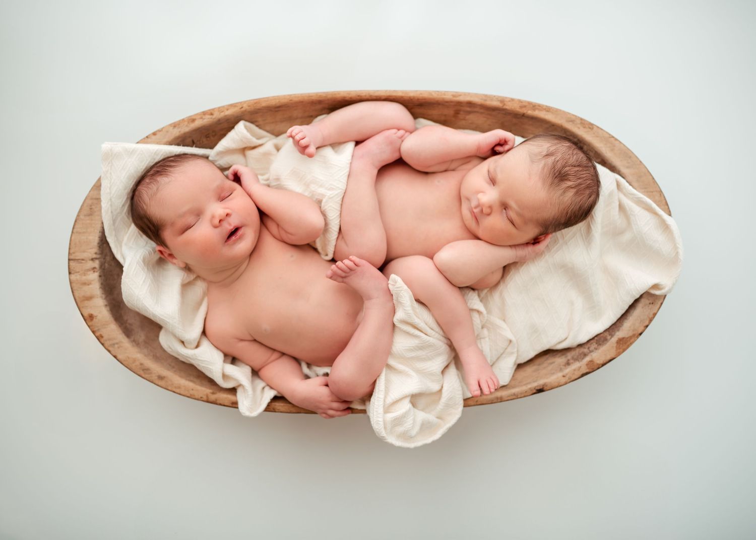 Sleeping newborn twins posed together in wooden bowl during studio newborn photography session in Florence, SC.
