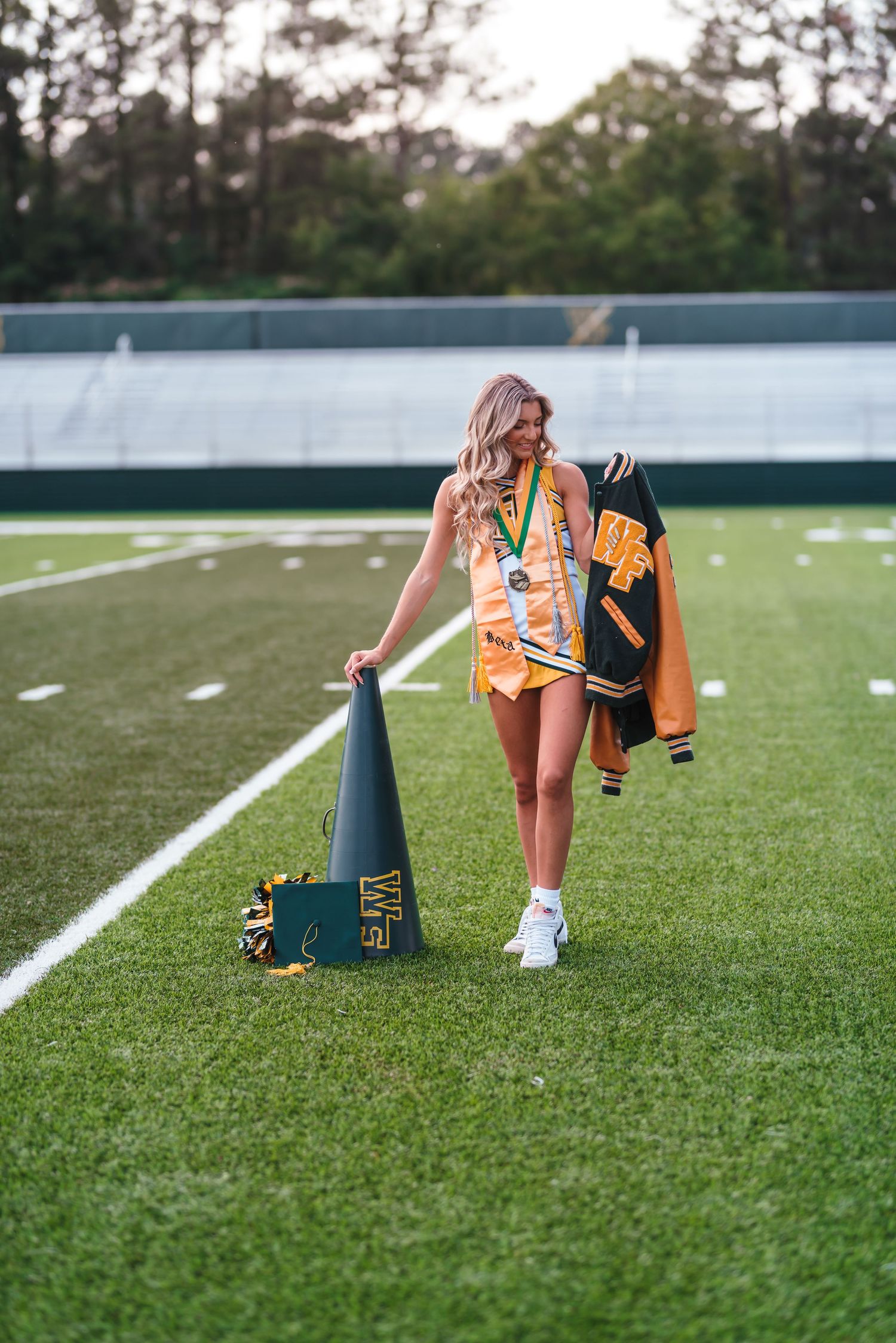 Cheerleader walking on football field carrying pom poms and megaphone.