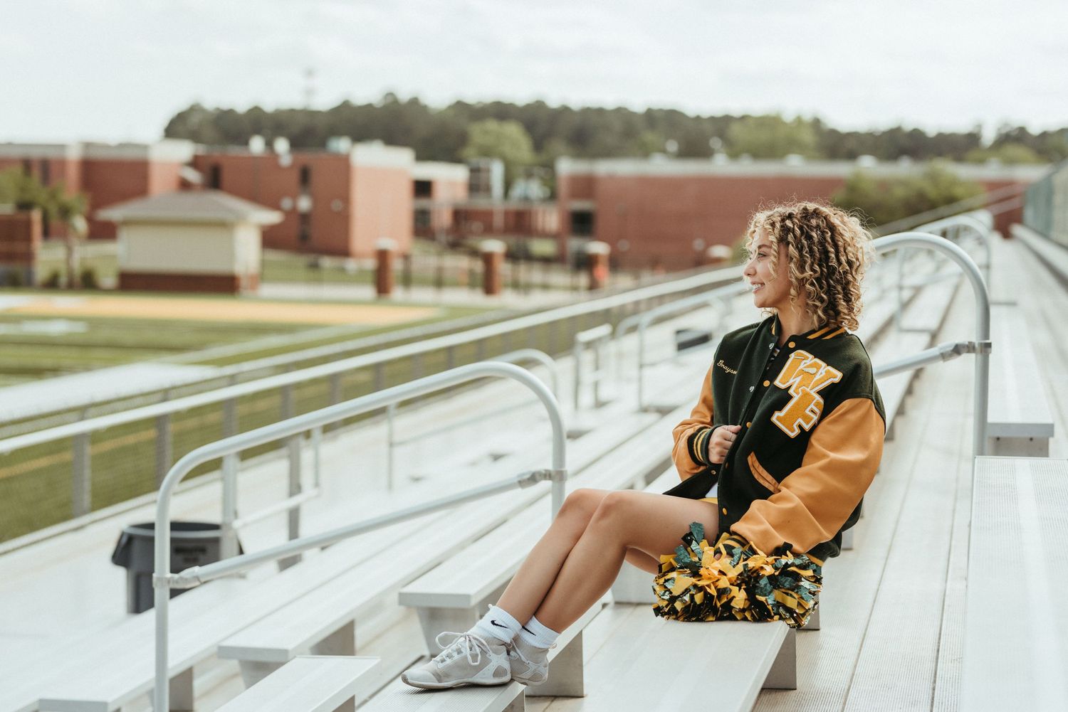 Person in varsity jacket sitting on bleachers at sports stadium.