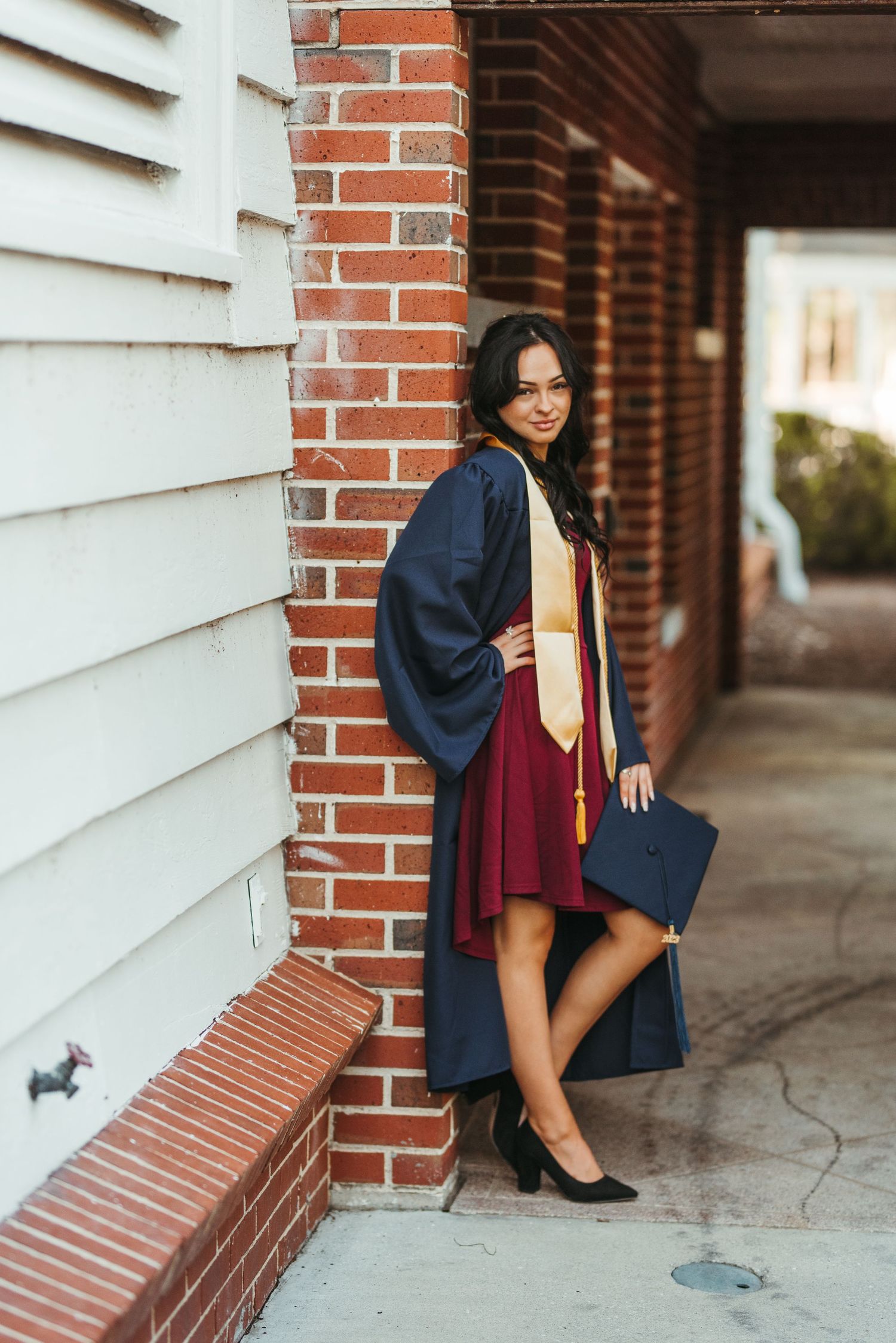 Creative graduation photo shoot by brick wall with navy cap and gown.