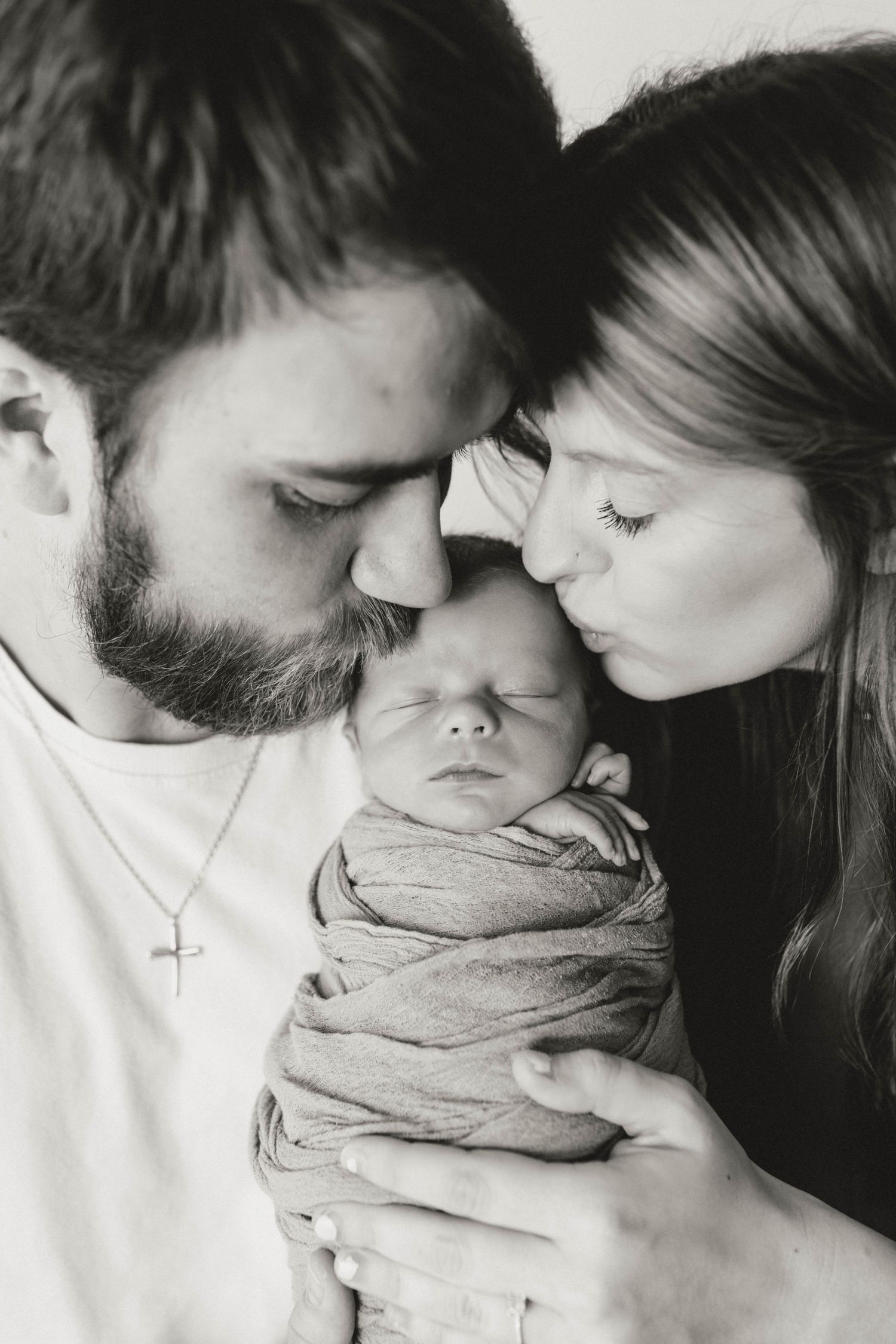 Intimate black and white portrait of new parents cradling their swaddled newborn.