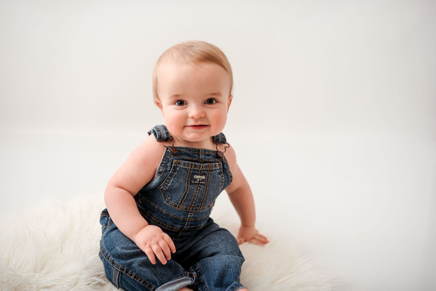 Baby in denim overalls sitting during studio portrait session.