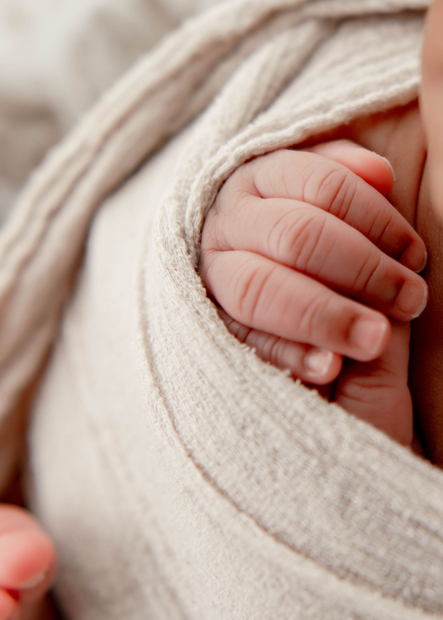Close-up of tiny baby fingers grasping soft cream-colored blanket texture.