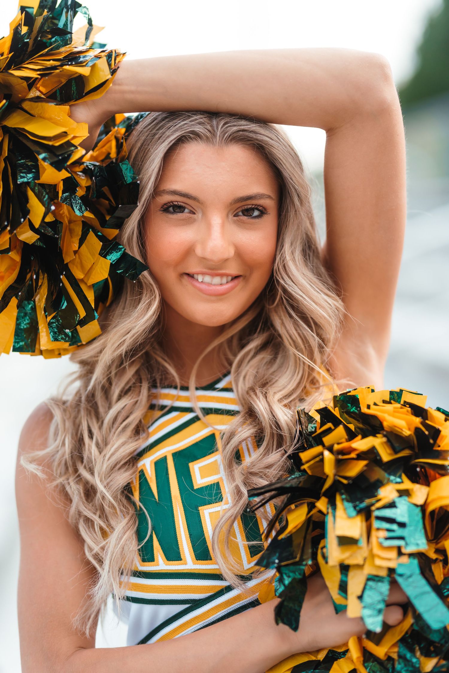 Cheerleader in green and gold uniform holding pom poms.