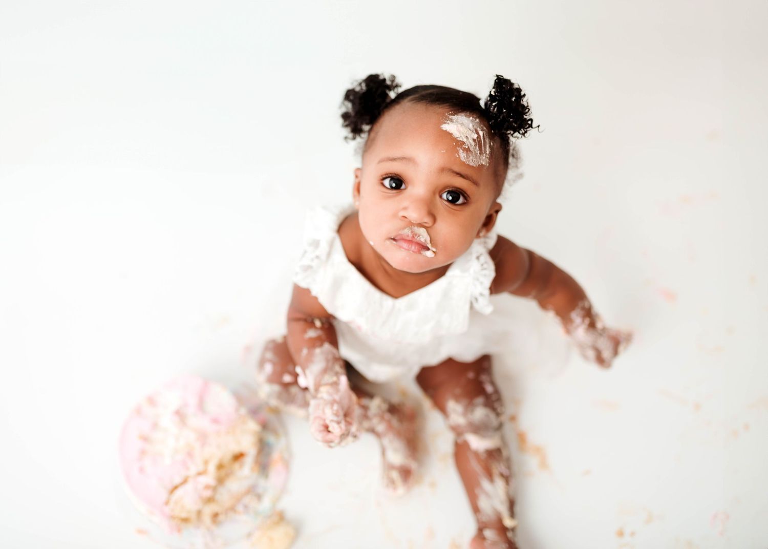 Newborn baby wearing a bow lies on white backdrop during professional photo session.