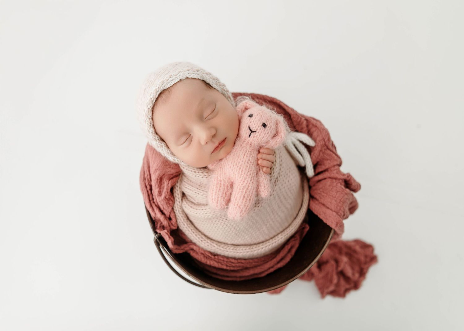 Newborn photography setup with soft pink and brown props on white background.