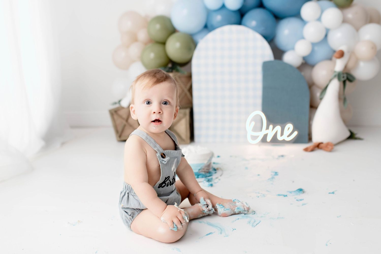 Cake smash photo setup with blue and white balloons and grid backdrop.